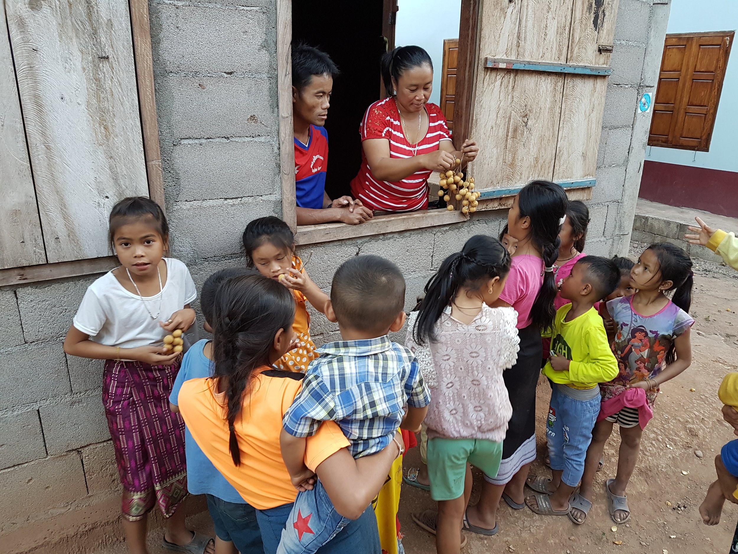 Une femme distribue des fruits à un groupe d'enfants devant une maison en construction.