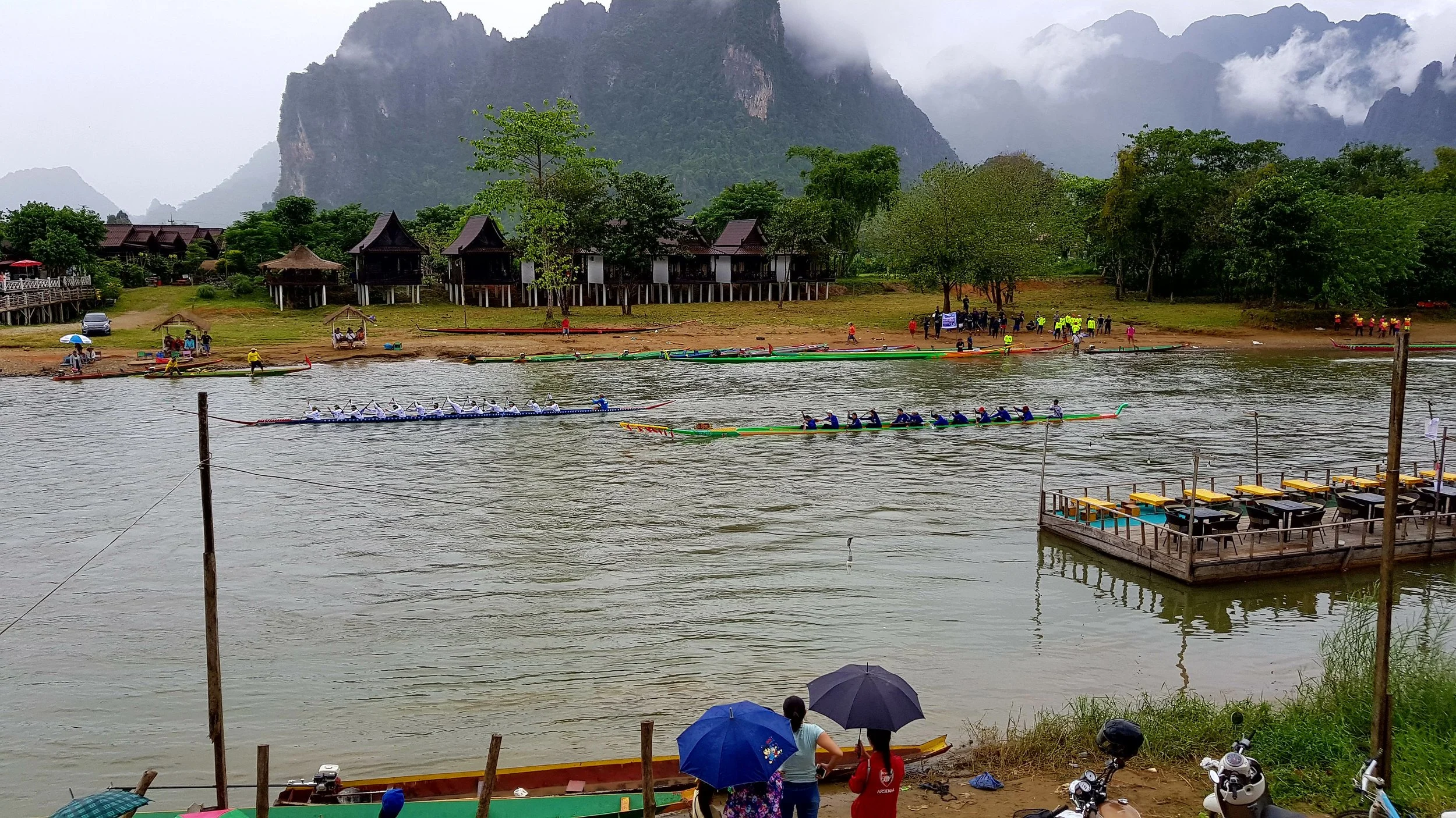 Course de bateaux traditionnels sur une rivière entourée de nature verte et de montagnes brumeuses.