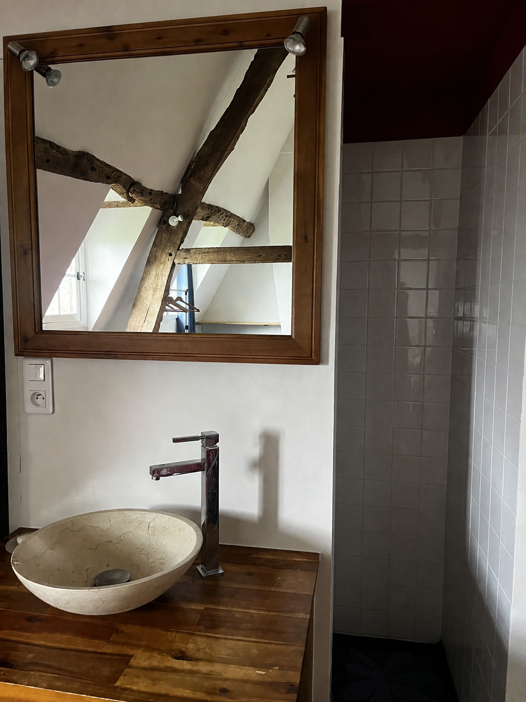 Un miroir au-dessus d'un lavabo en pierre sur une surface en bois, reflet d'une pièce avec poutres en bois et fenêtres dans une salle de douche, retraite en normandie septembre 2026, charme de l'ancien