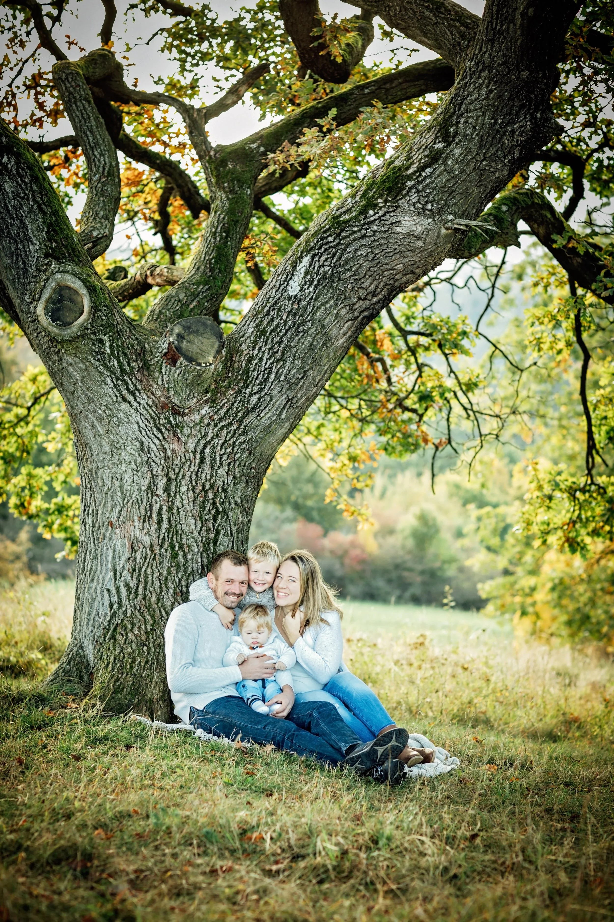 Familie mit zwei Erwachsenen und zwei Kindern unter einem großen Baum im Park, im Herbst, entspannen und lachen.