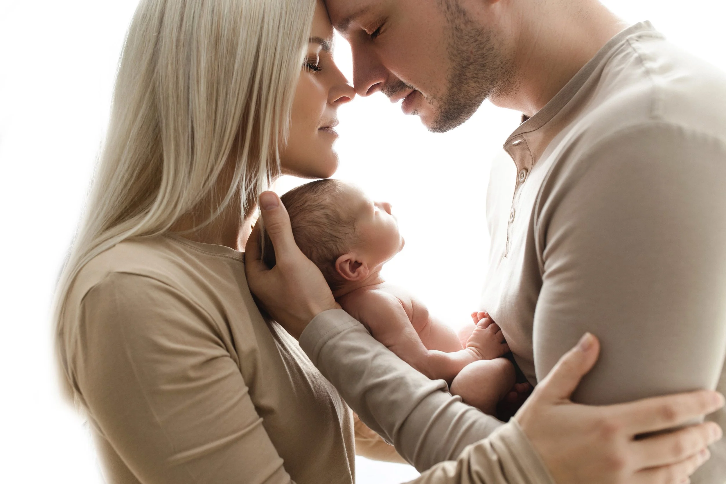 Ein Mann und eine Frau halten ein neugeborenes Baby zwischen sich und berühren ihre Stirn.