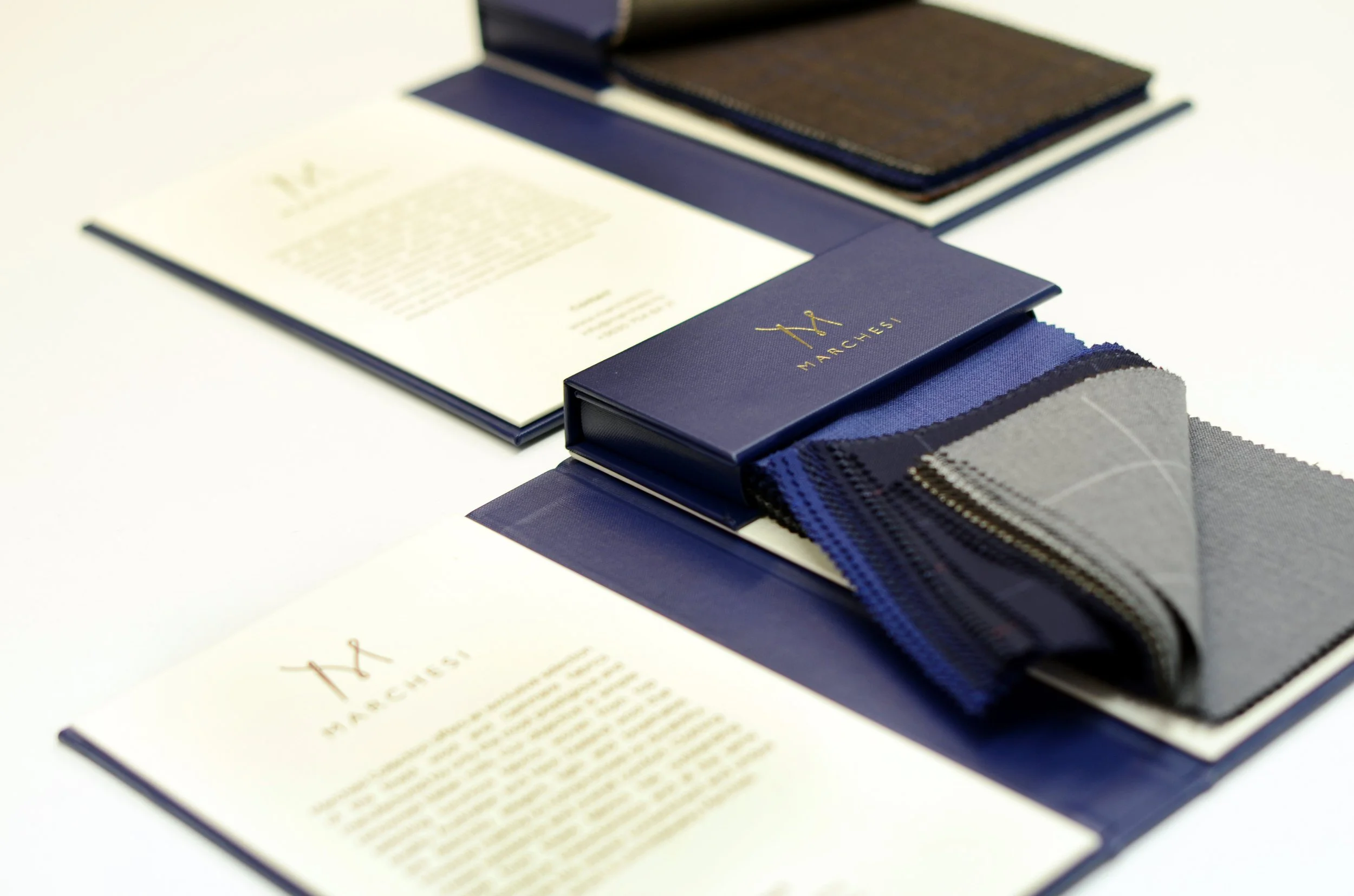 Close-up of fabric swatches and a blue box with the name 'Marchex' on it, used for selecting textiles, with a focus on dark blue, gray, and other fabric samples.