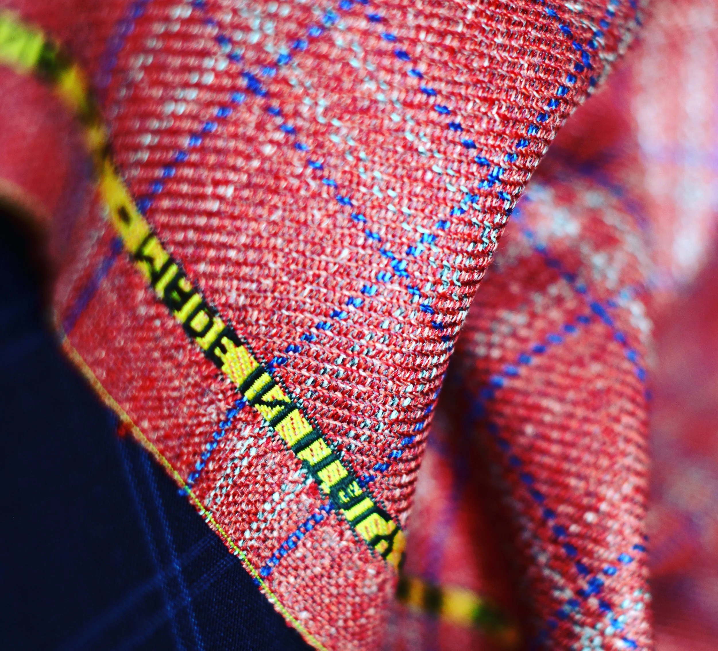 Close-up of red textured fabric with small blue and white details and black and yellow embroidered text along the edge.