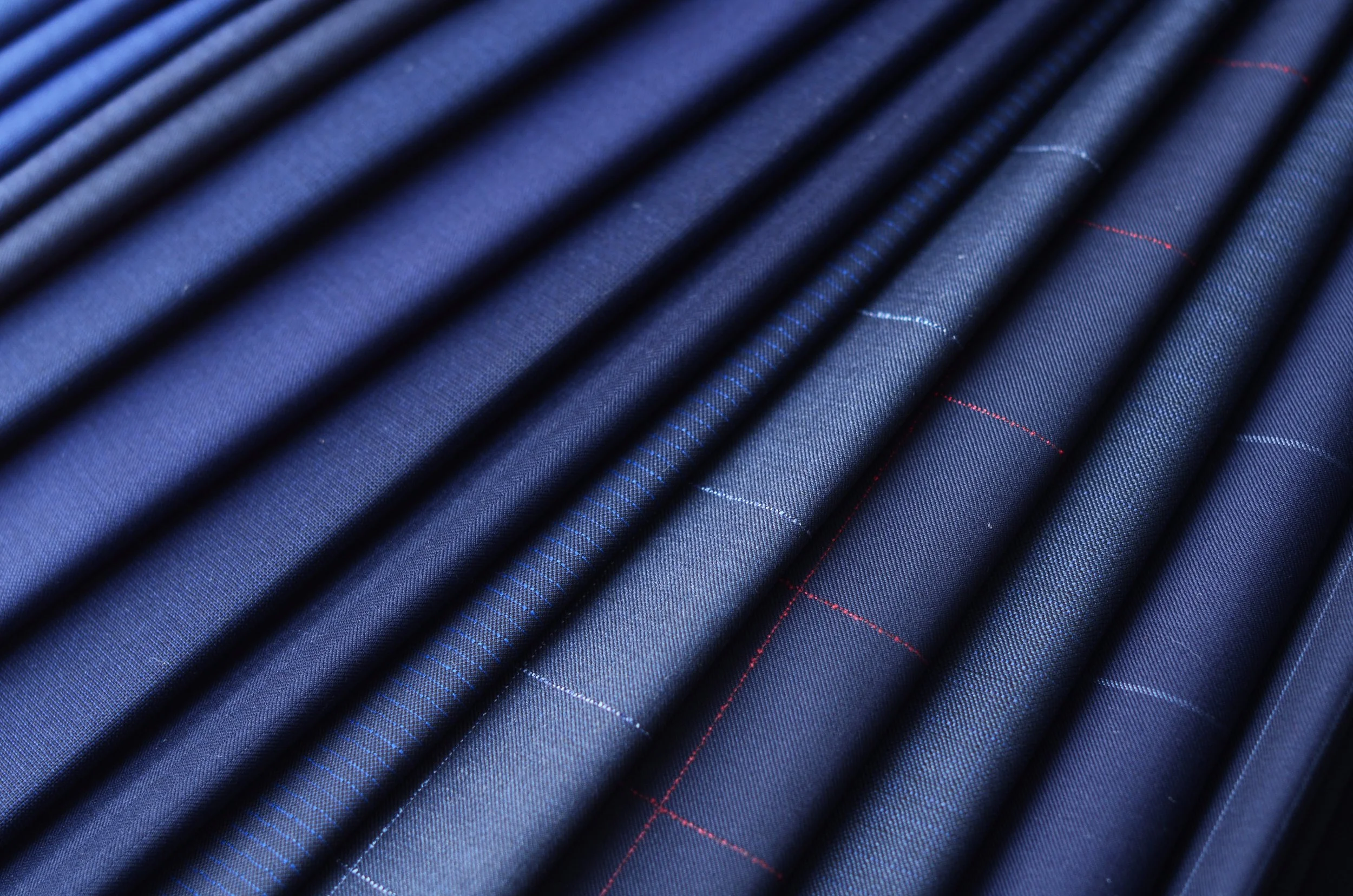 Close-up of dark blue fabric with red and blue thread stitching, arranged with pleats.
