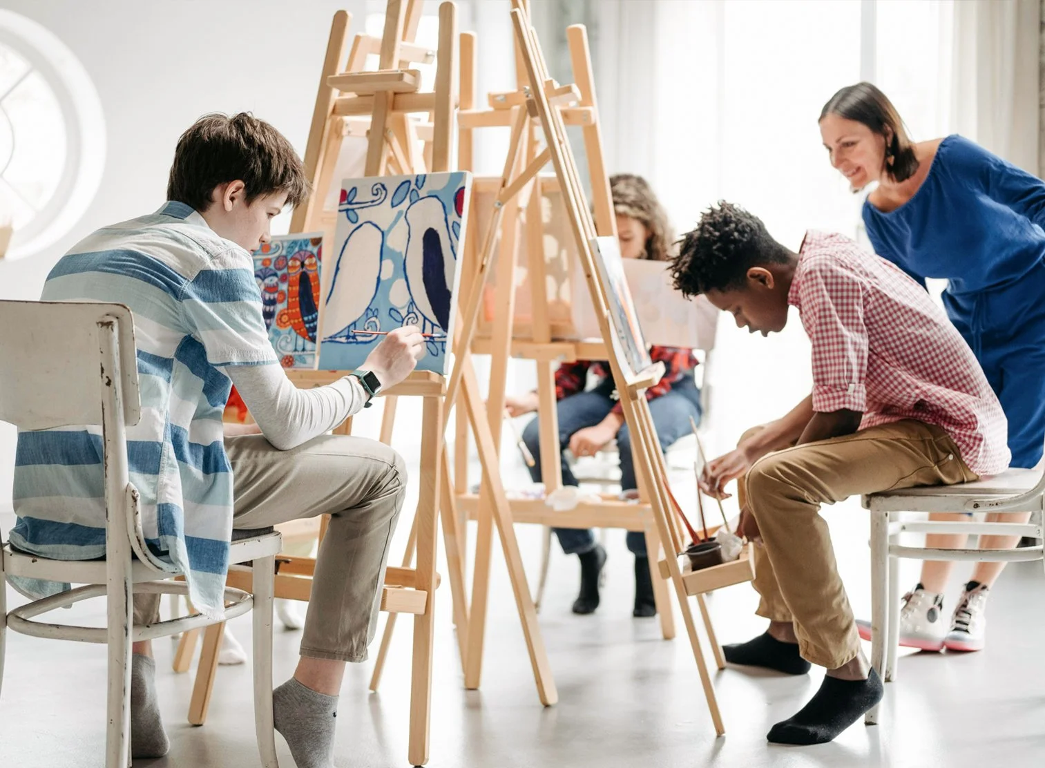 A group of young people participating in a painting class in a bright, airy studio, painting colorful artwork with easels.
