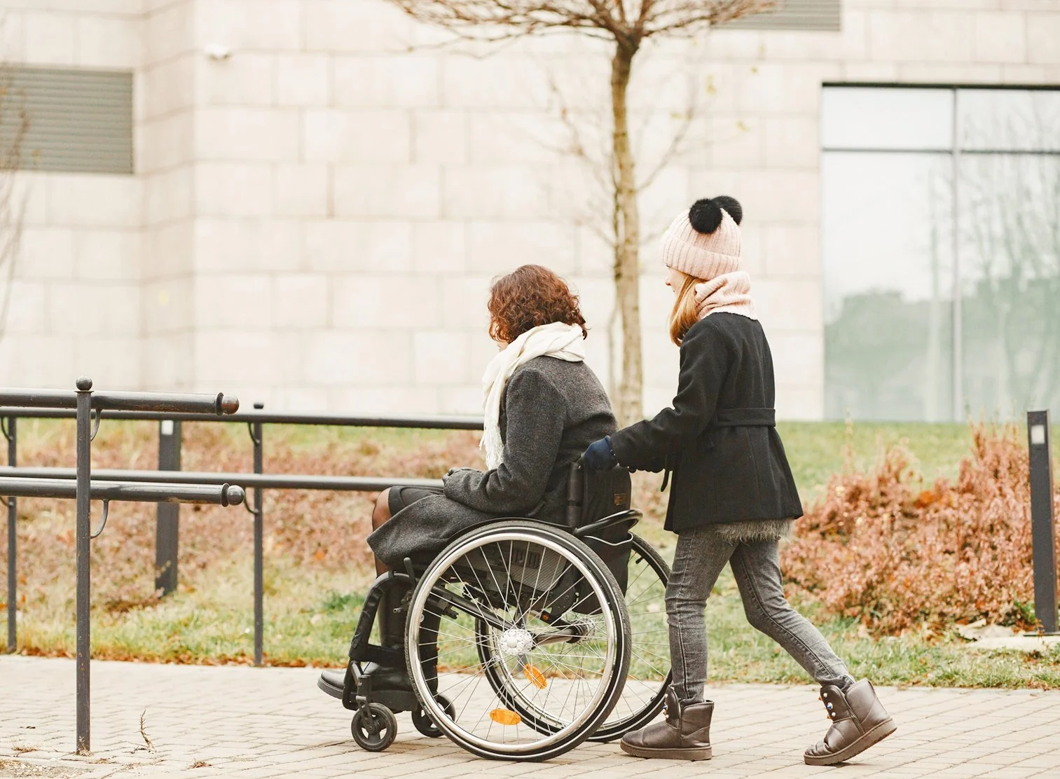 Support worker assisting a wheelchair user on an outdoor paved pathway