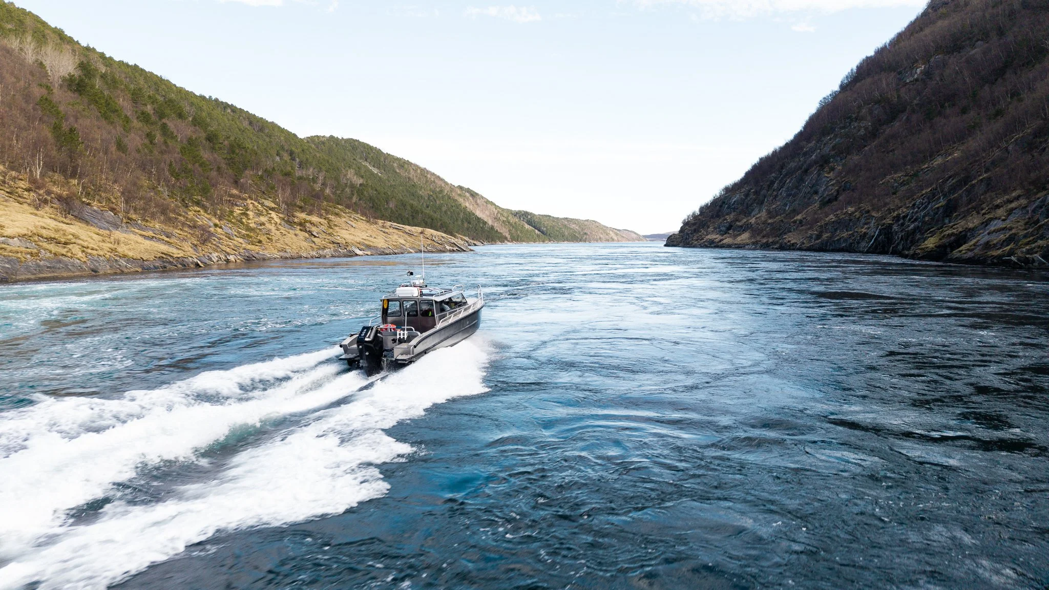 Fjord med en motorbåt som kjører mellom fjell, med vann og naturlandskap på sidene.