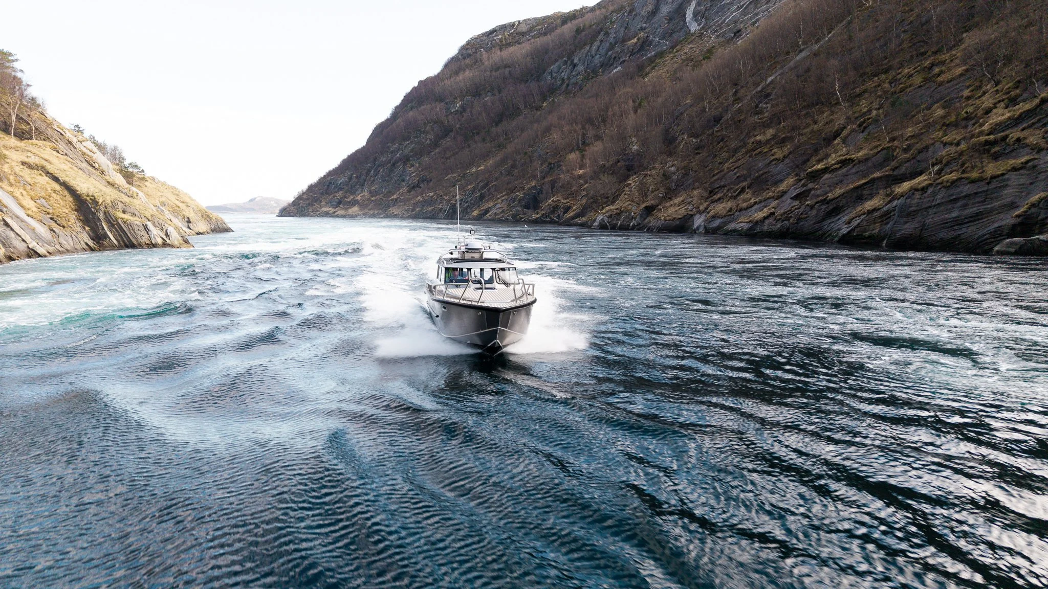 En båt som kjører gjennom en smal fjord omgitt av bratte åssider med lite vegetasjon.