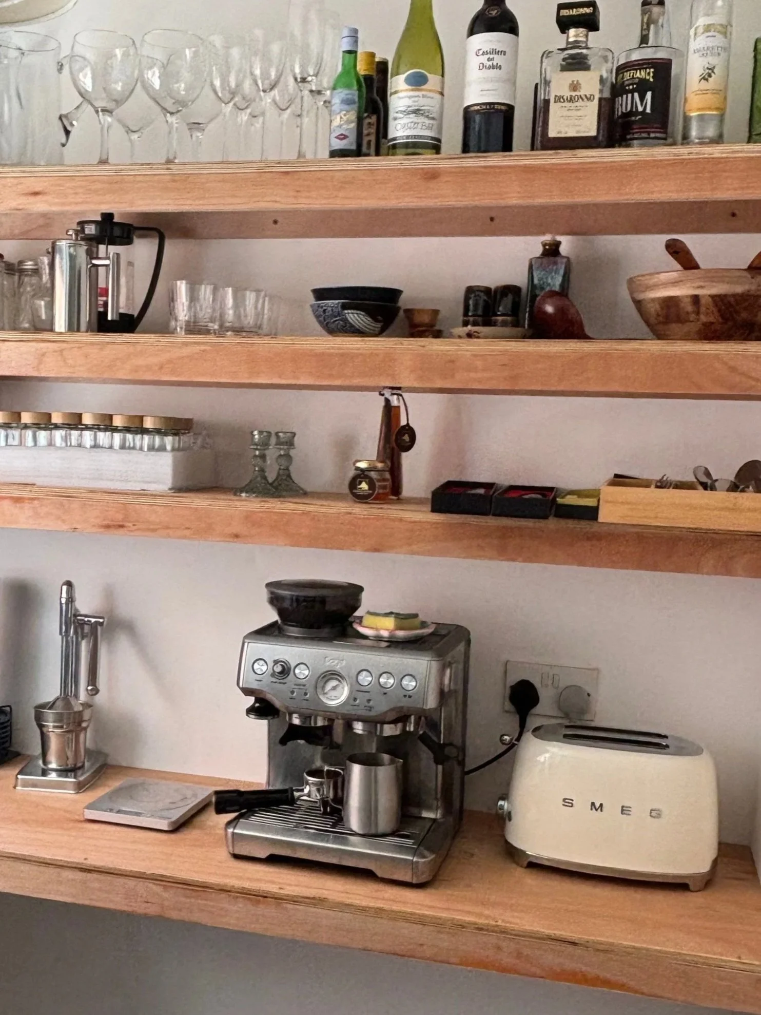 Kitchen shelves with glassware, bottles of wine and liquor, bowls, jars, a coffee maker, and a toaster.