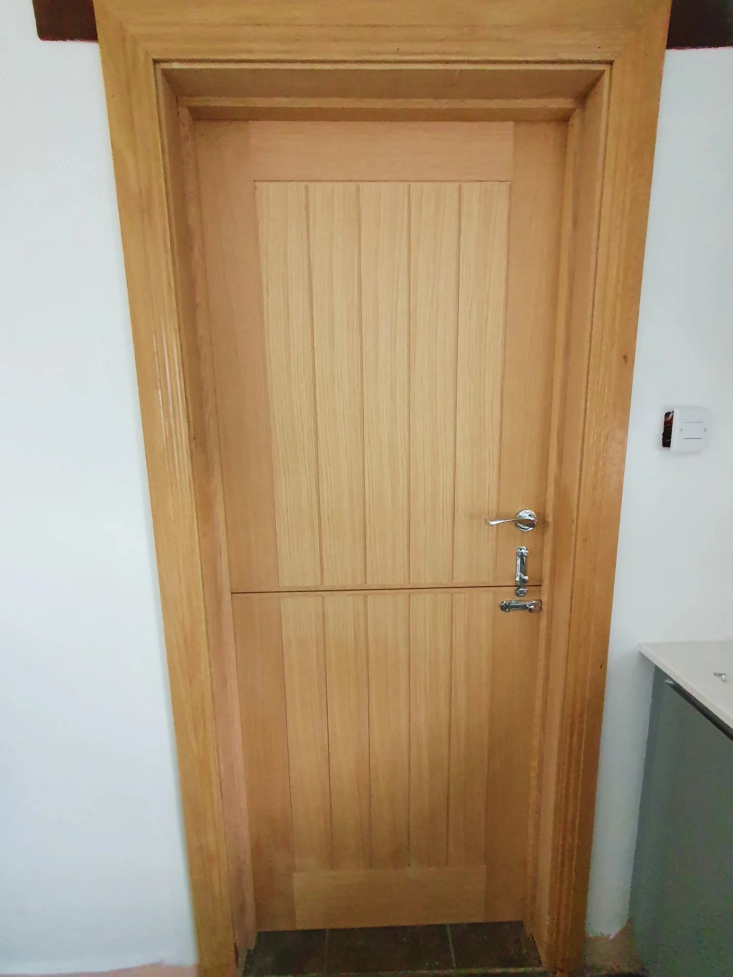 A closed wooden door with vertical panels and a silver handle, set in a wooden frame against a white wall, with a small white radiator visible to the right.