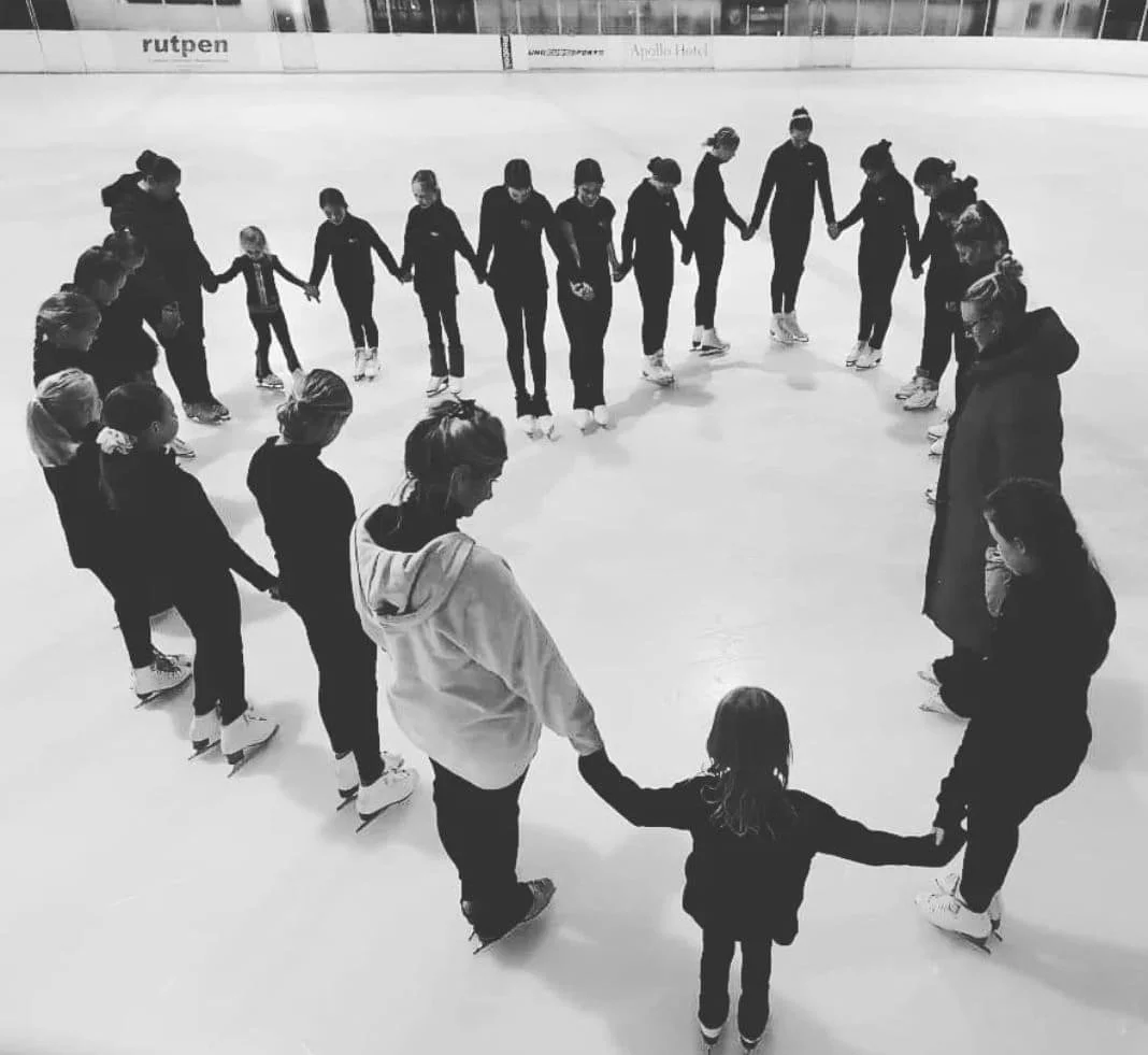 A group of people, including children and adults, standing in a large circle on an ice rink.