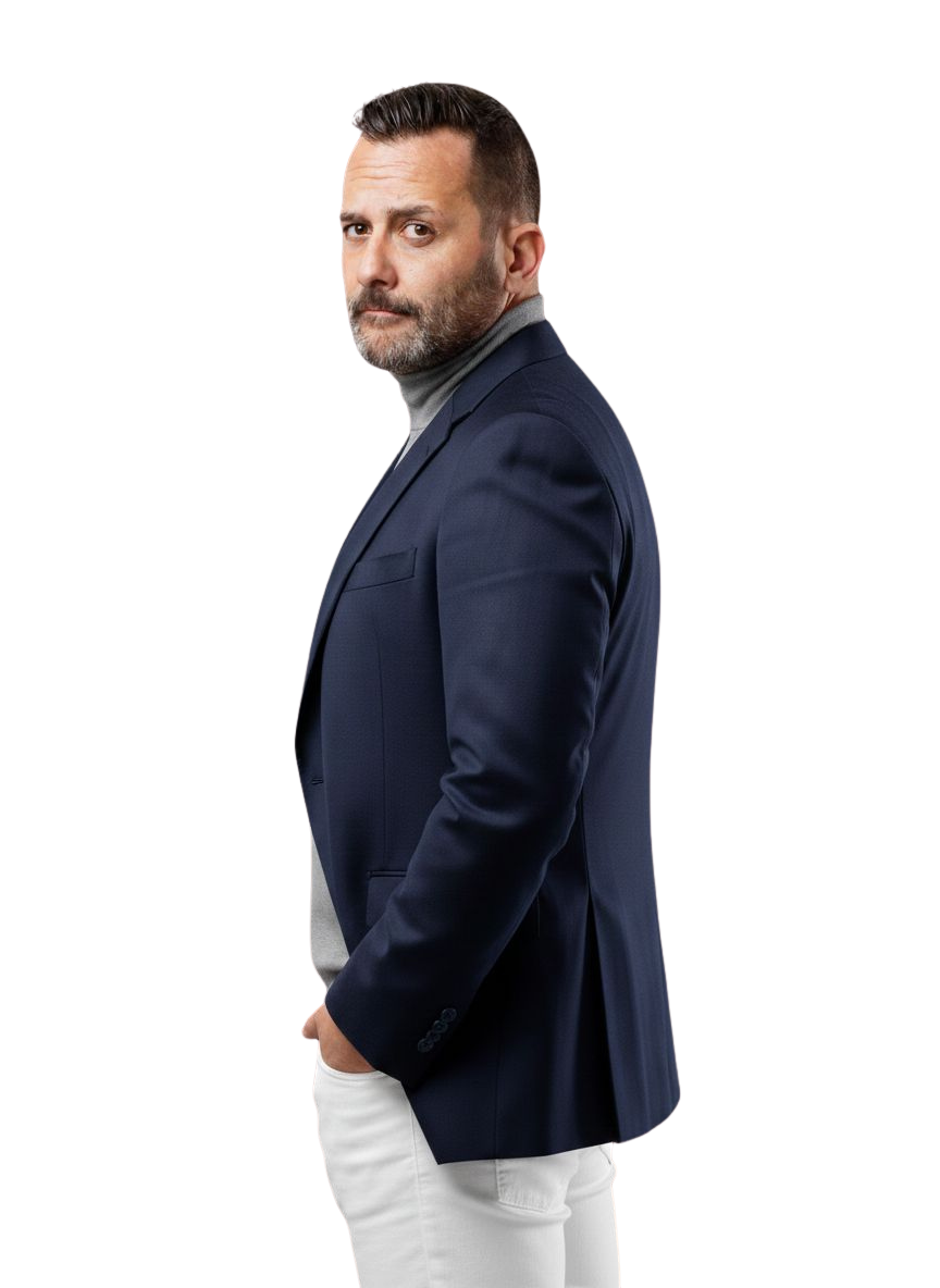 Hombre con barba y cabello corto, vestido con saco azul y camiseta gris, posando de perfil con expresión seria