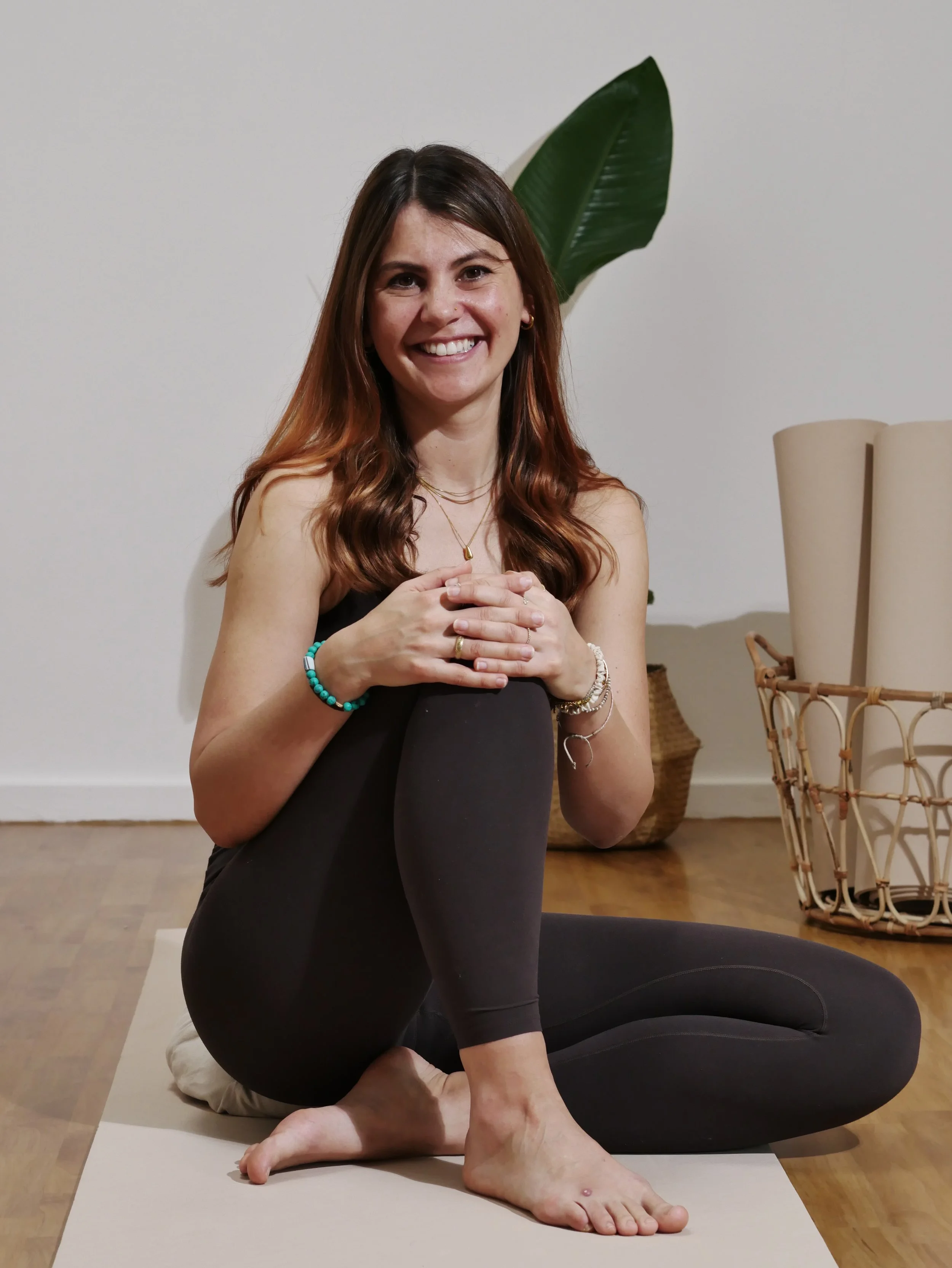 Melanie Dosch sitzt in einem Yoga-Studio mit Pflanzen und Korbwaren im Hintergrund.