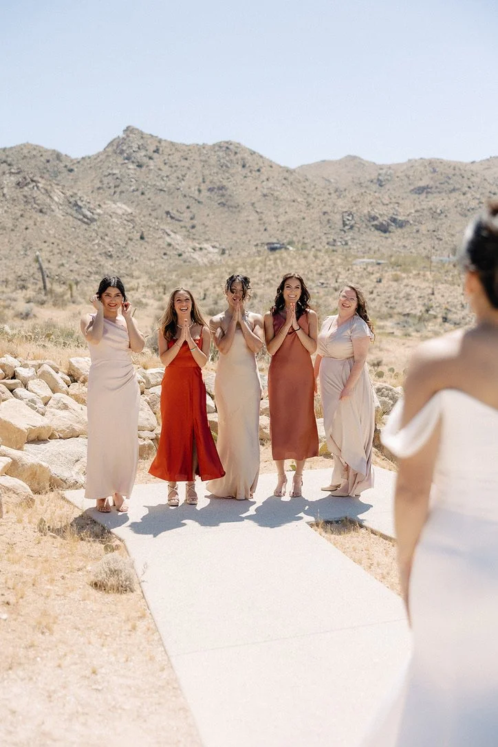 bridesmaids in earth tone dresses reacting to the bride's outfit and makeup in a Jasper and Lane Events Palm Springs wedding.