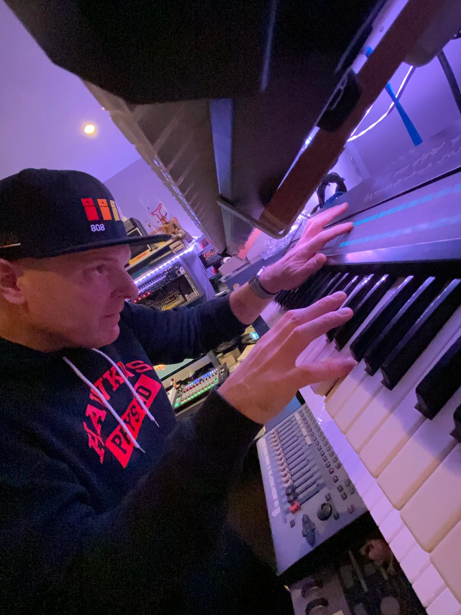 James Hockley wearing a black hoodie and a cap playing a keyboard synthesizer