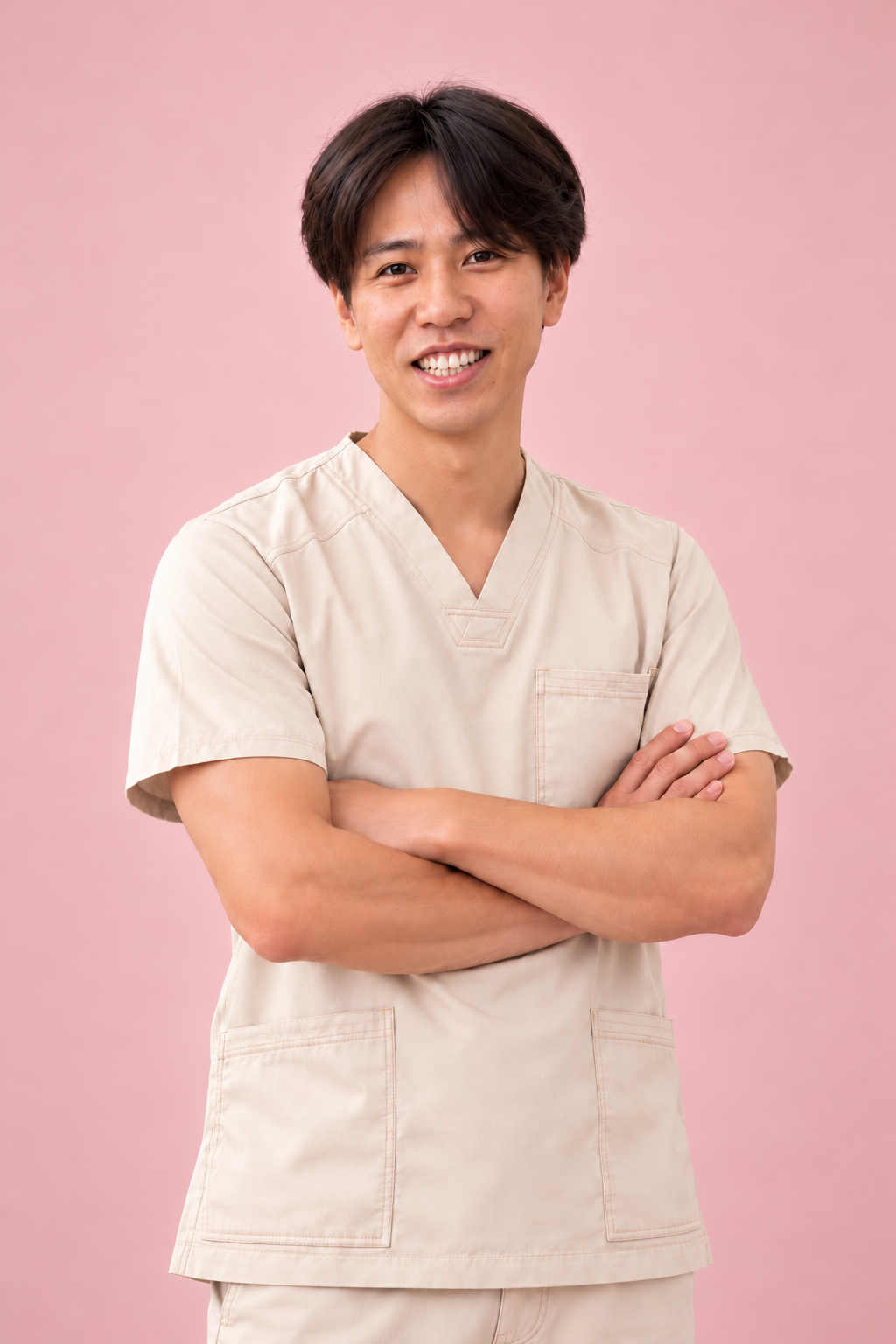A smiling man in medical scrubs with arms crossed, standing against a pink background.