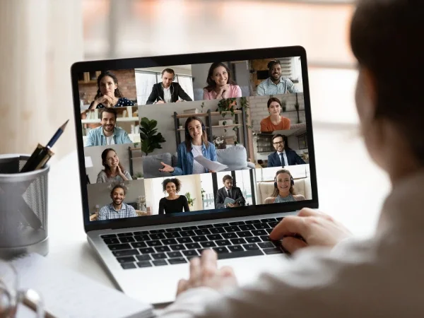 A person participating in a virtual meeting on a laptop with multiple people displayed in a grid on the screen.