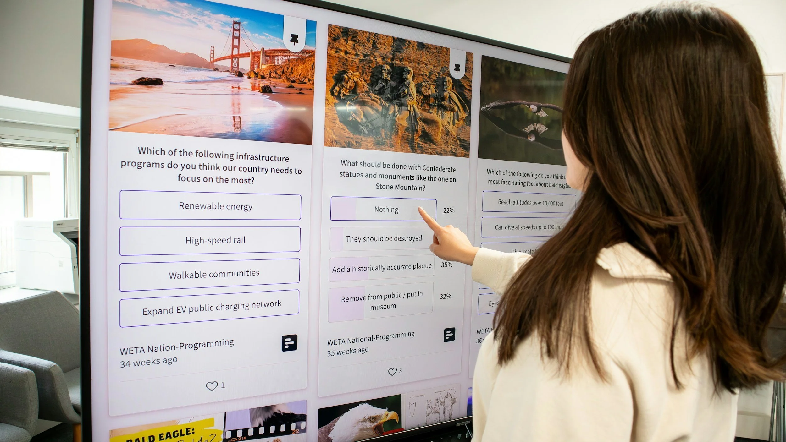 A woman with brown hair pointing at a screen displaying a survey about infrastructure programs and monuments. The screen shows images of the Golden Gate Bridge, Confederate statues, and a bald eagle, with questions and multiple-choice options.