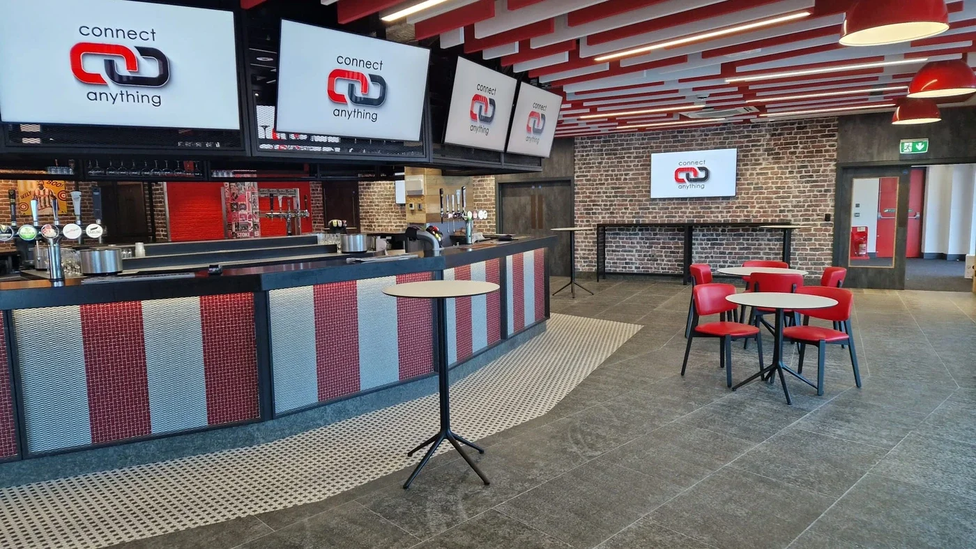 Interior of a modern bar or restaurant with a bar counter, multiple LED screens displaying