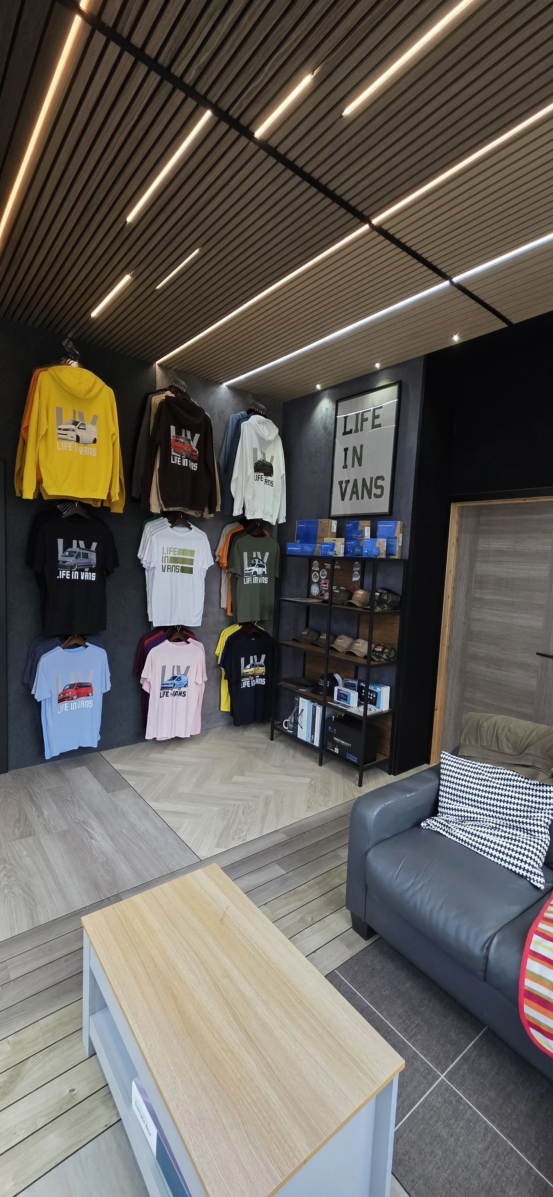 Display of Vans hoodies and T-shirts with car graphics in a retail store, with a sign reading 'Life in Vans' on the wall.