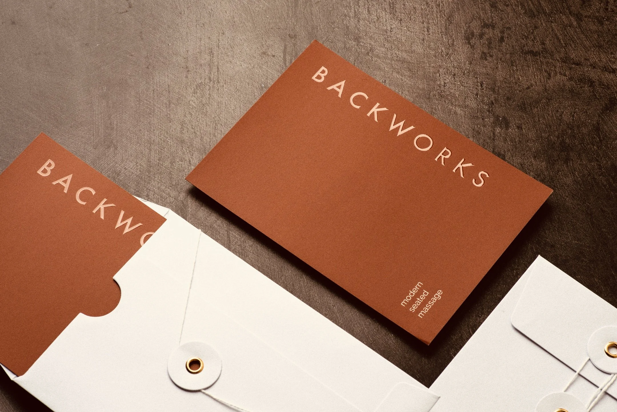 Business cards with the words "BACKWORKS" and descriptions of massage services placed on a dark wooden surface.