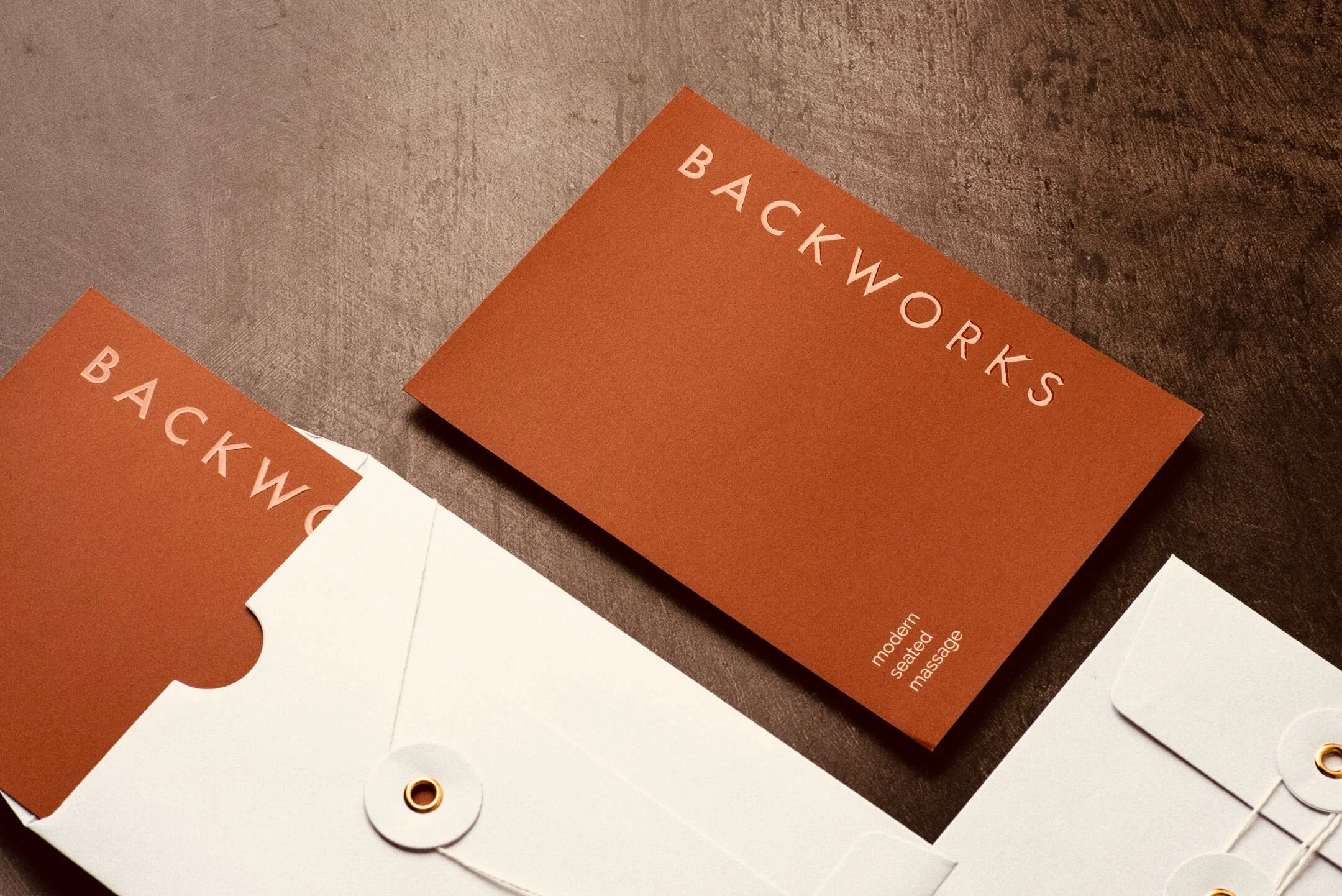 Close-up of product packaging labels for BackWorx, a modern, heated, seated massage device, in orange and white, on a dark textured surface.