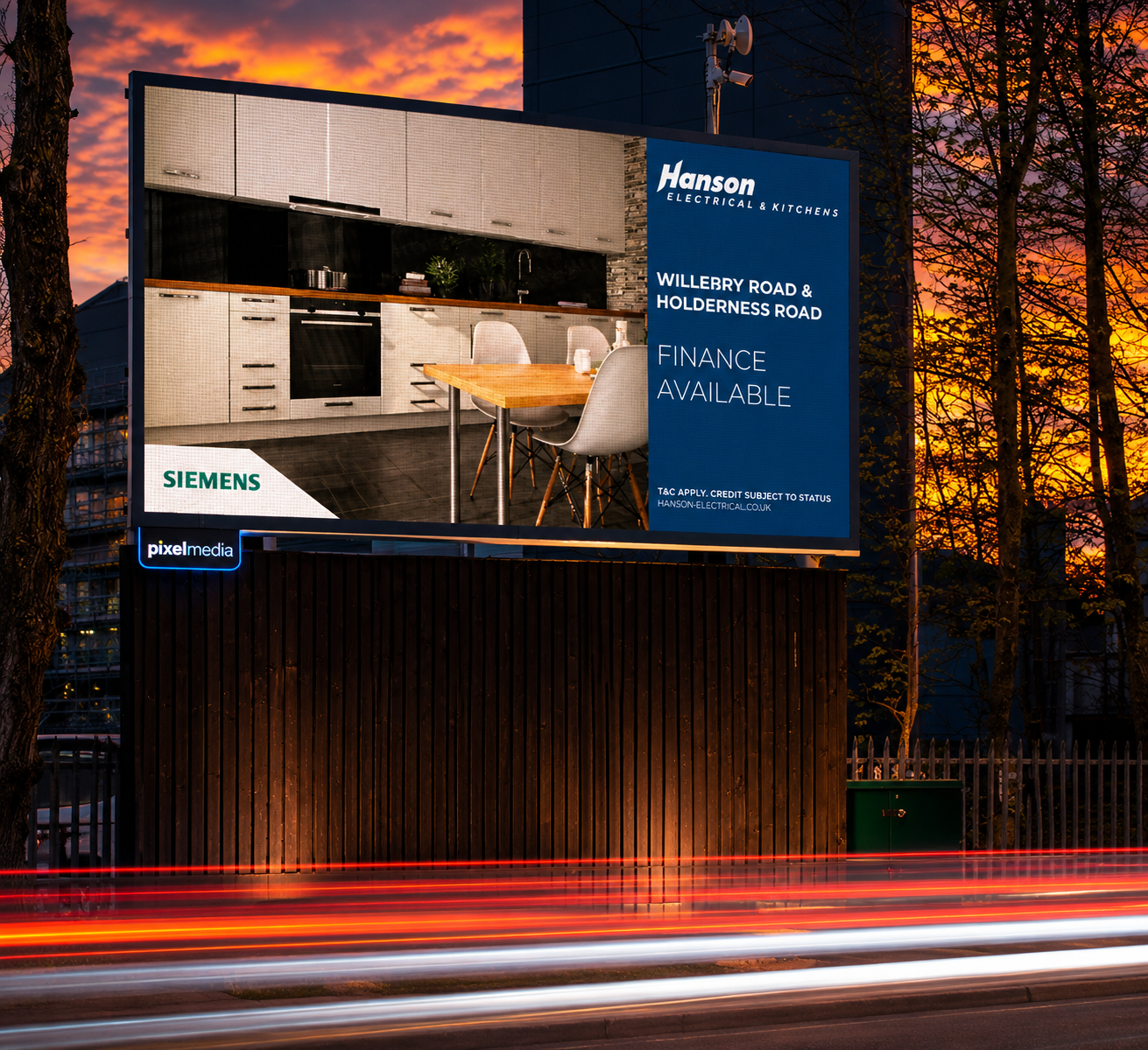 A large outdoor advertising billboaord at sunset, displaying an interior kitchen with white cabinets, a wooden dining table, and modern chairs. To the right, blue background with white text for Hanson Electrical & Kitchens, announcing location and finance options. Logos for Siemens and Pixel Media are at the bottom left and corner.