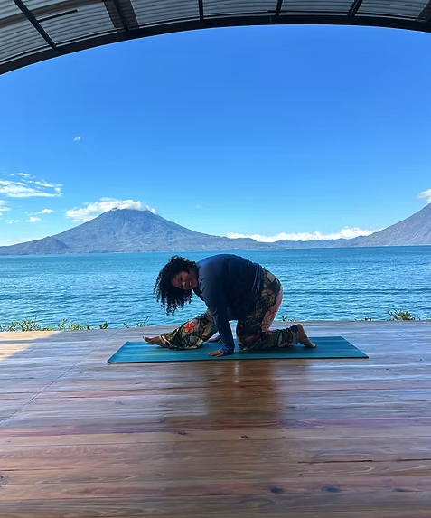 A person practicing yoga on a blue mat outdoors with a lake and mountains in the background.
