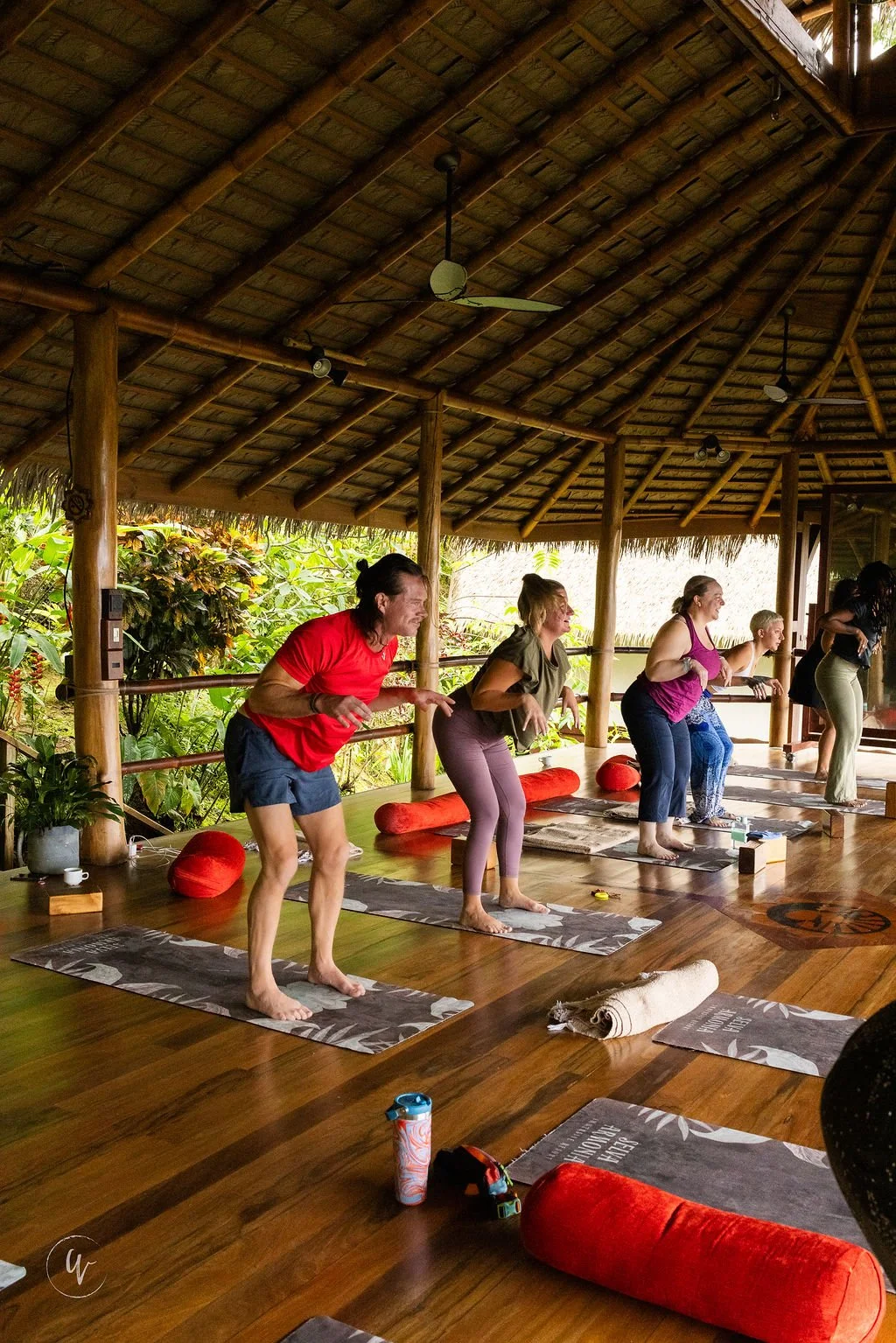 Group of people doing yoga in a bamboo shelter, with lush greenery outside.
