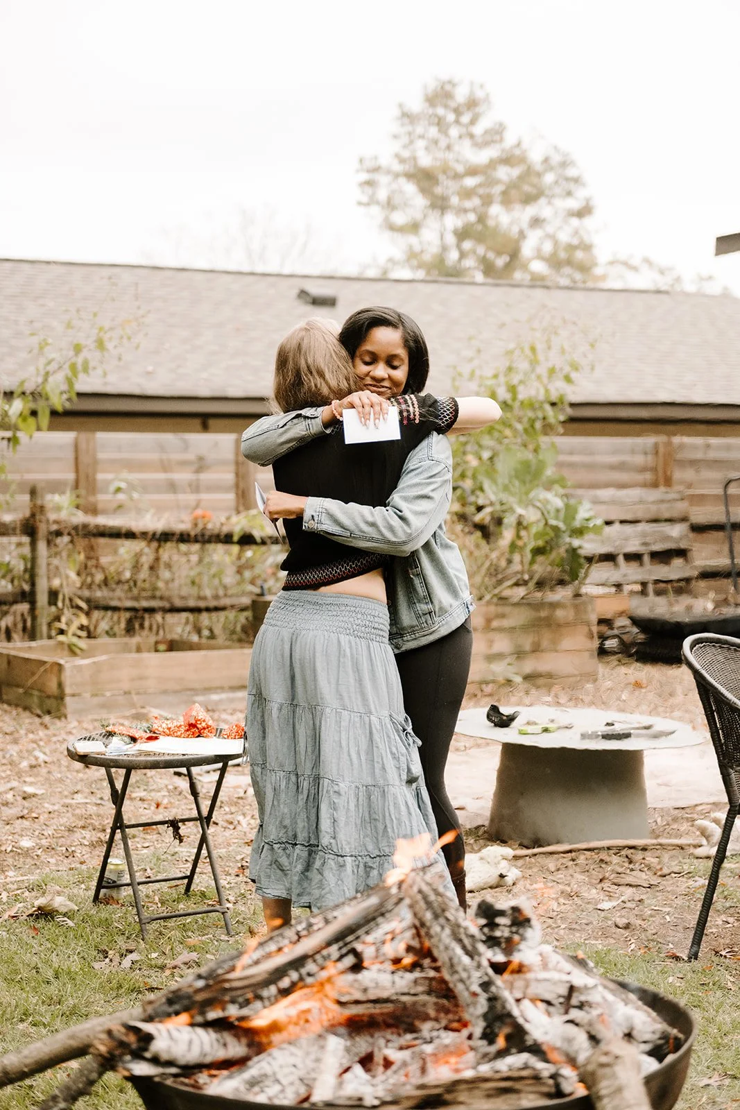 Two people hugging outdoors near a fire pit in a backyard.