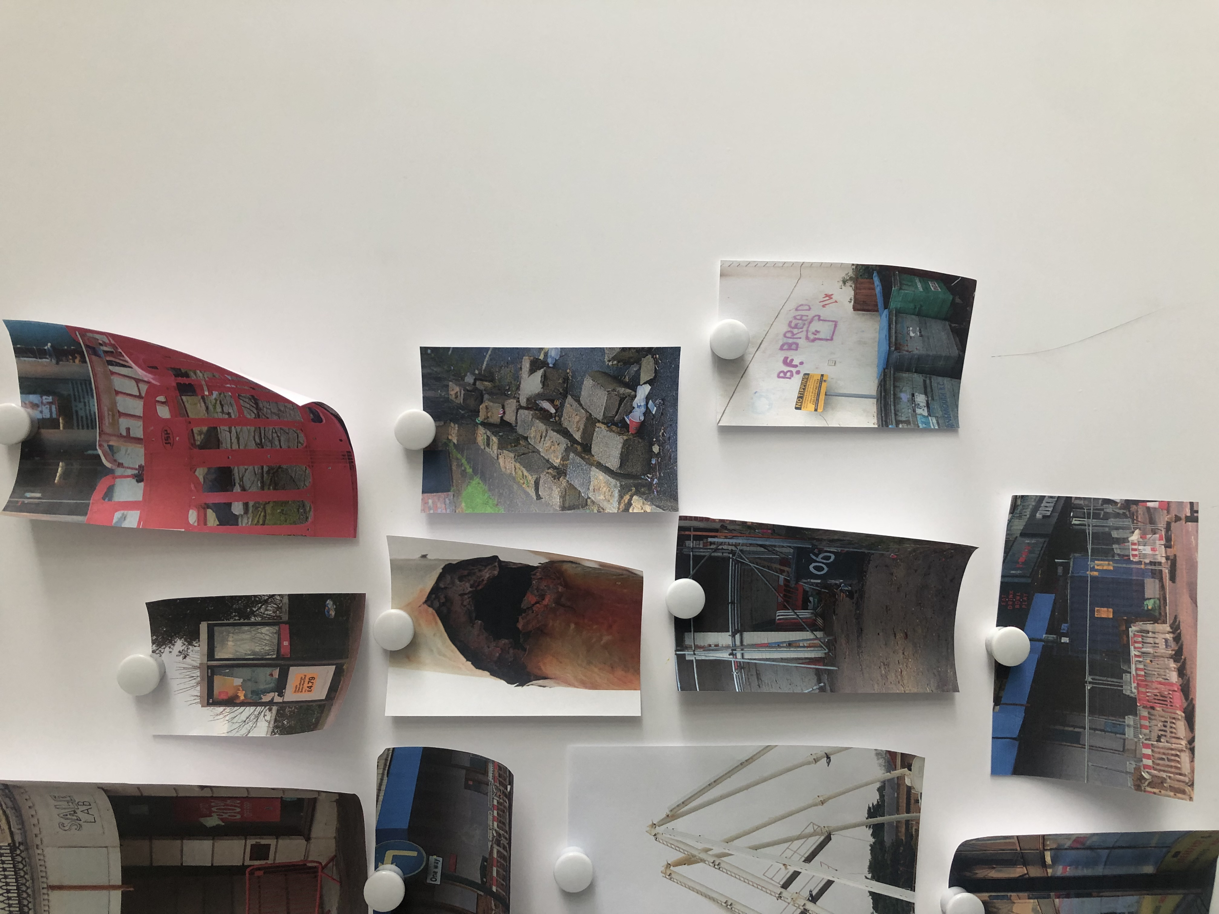 Photographs of city scenes and advertisements arranged on a whiteboard with white magnets.