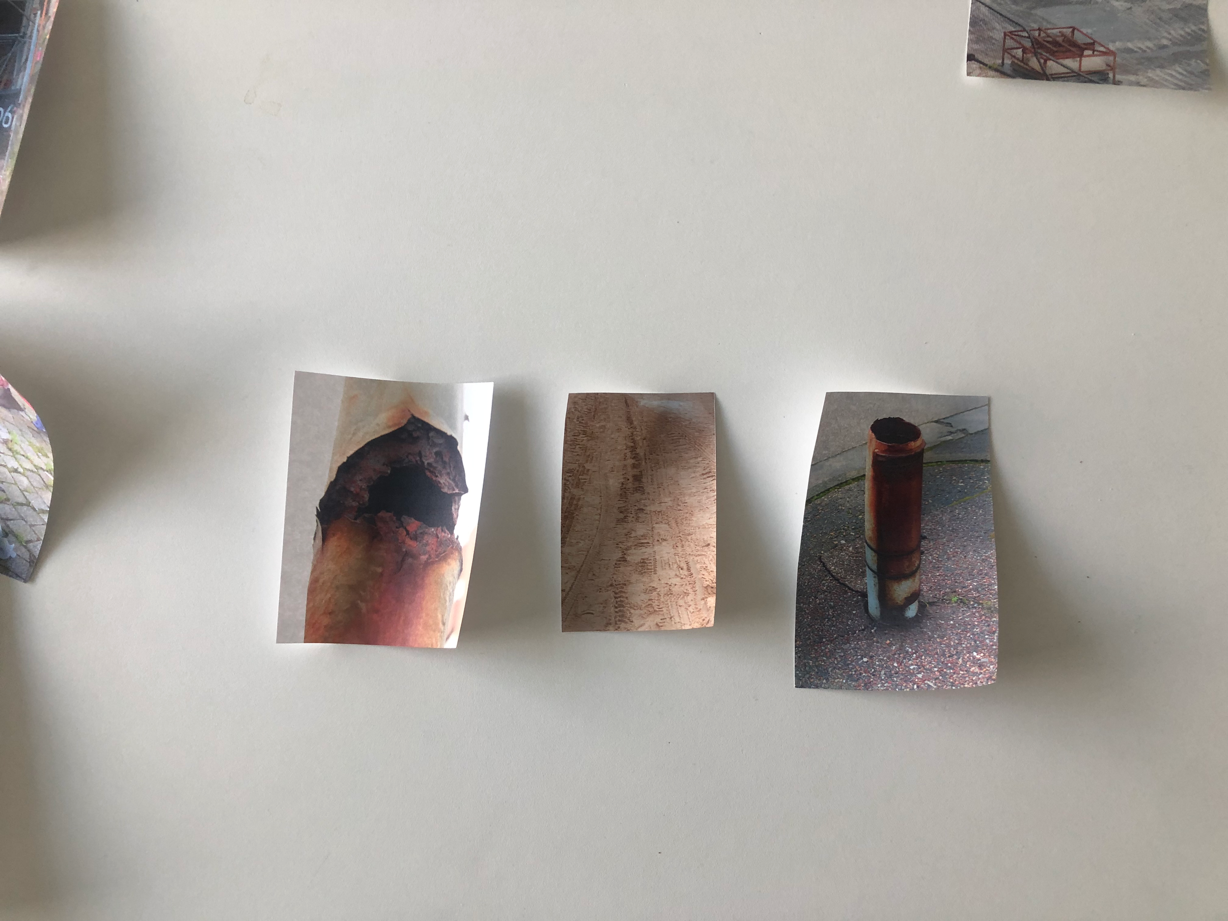 Several small photographs scattered on a white surface, each depicting different objects including a burning log, a wooden surface, and a rusty pipe connected to a chain-link fence.