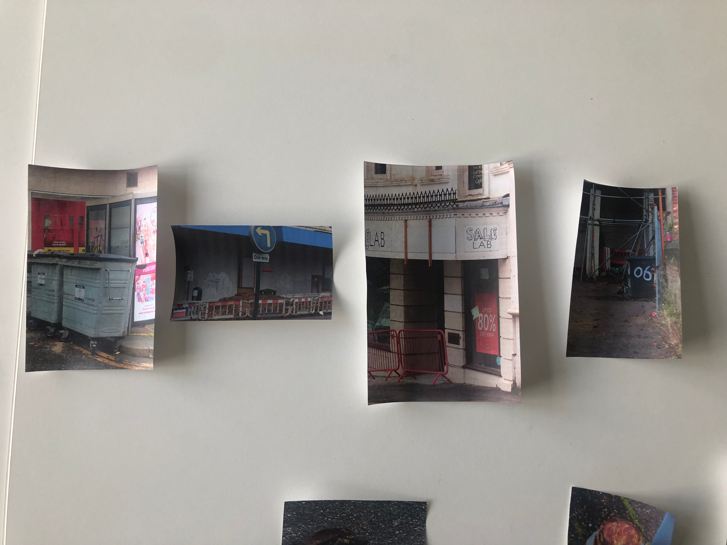 Photograph of a white wall with four cut-out photographs attached, showing city street scenes and storefronts.