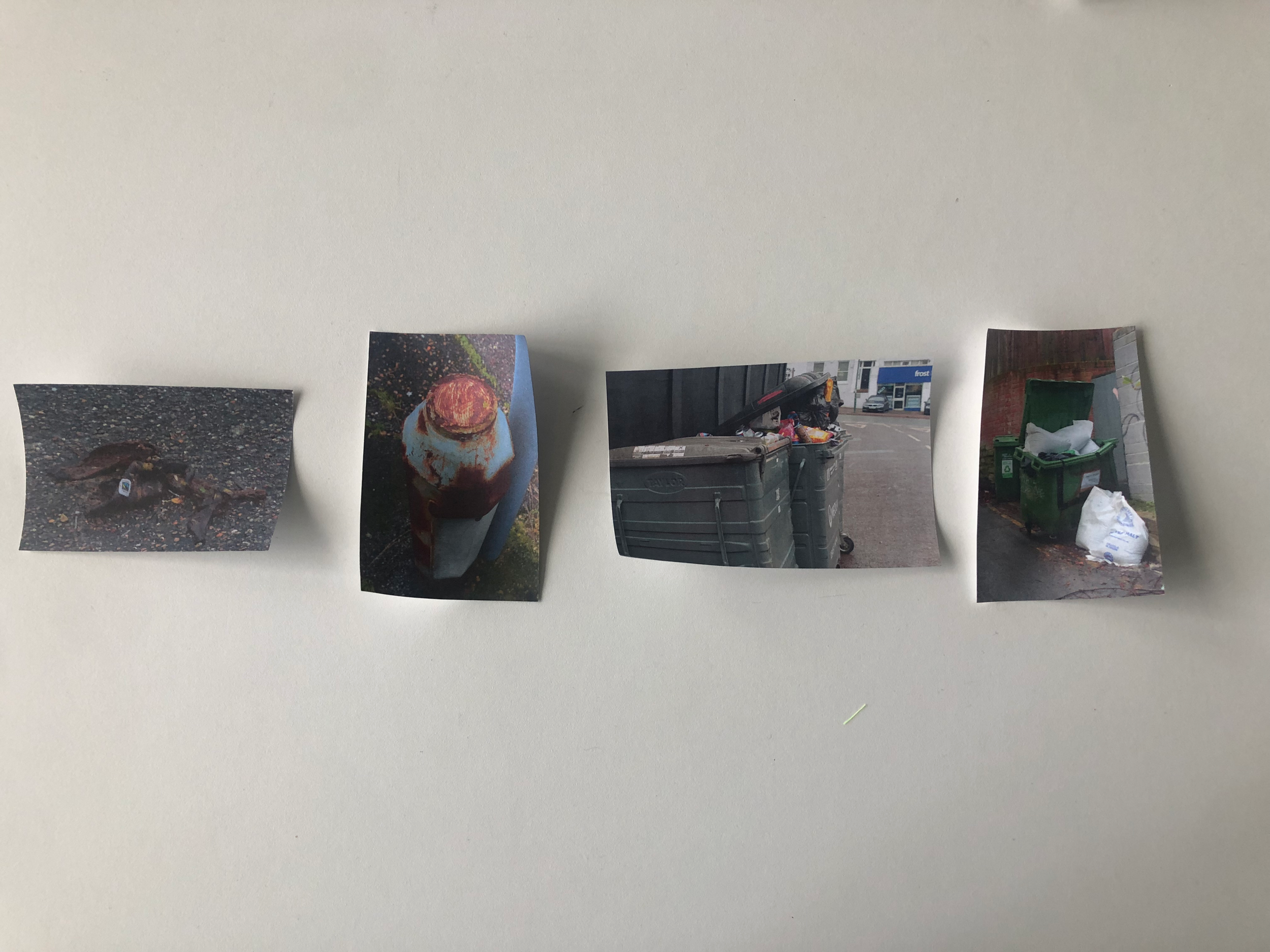 Photograph of four printed photographs taped to a white wall, featuring various trash and garbage scenes.