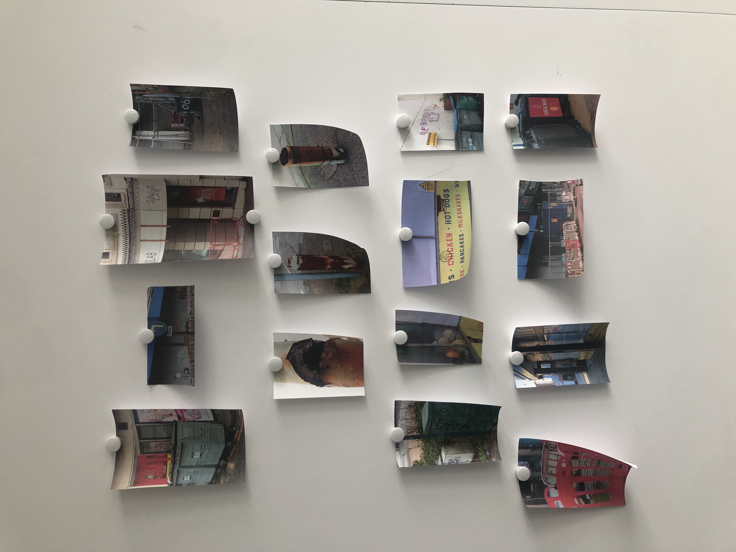 A wall with a collage of various printed photographs or postcards, pinned with white round magnets.