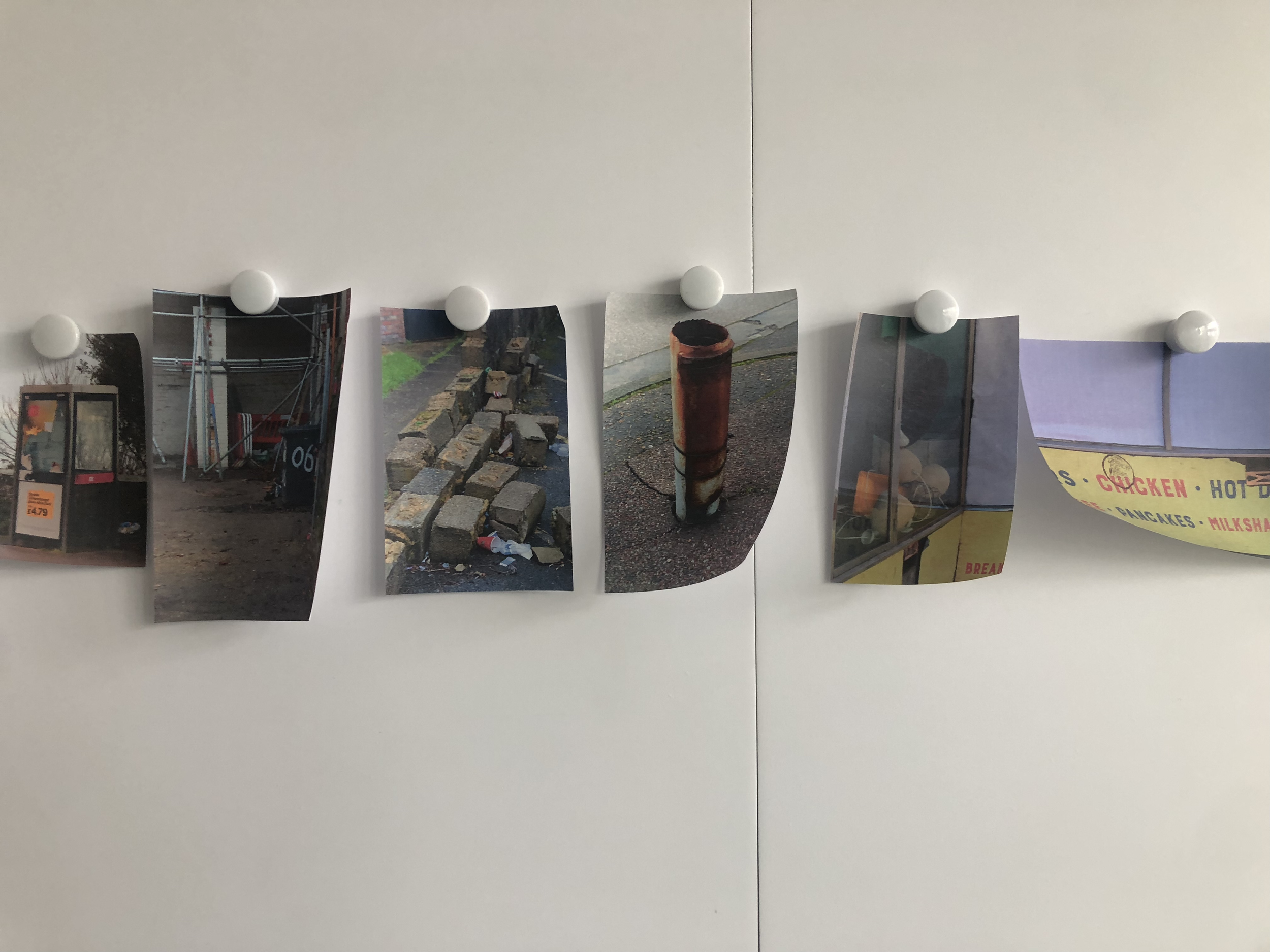 A series of printed photographs of outdoor scenes and objects are clipped to a string with white round magnets against a white wall.