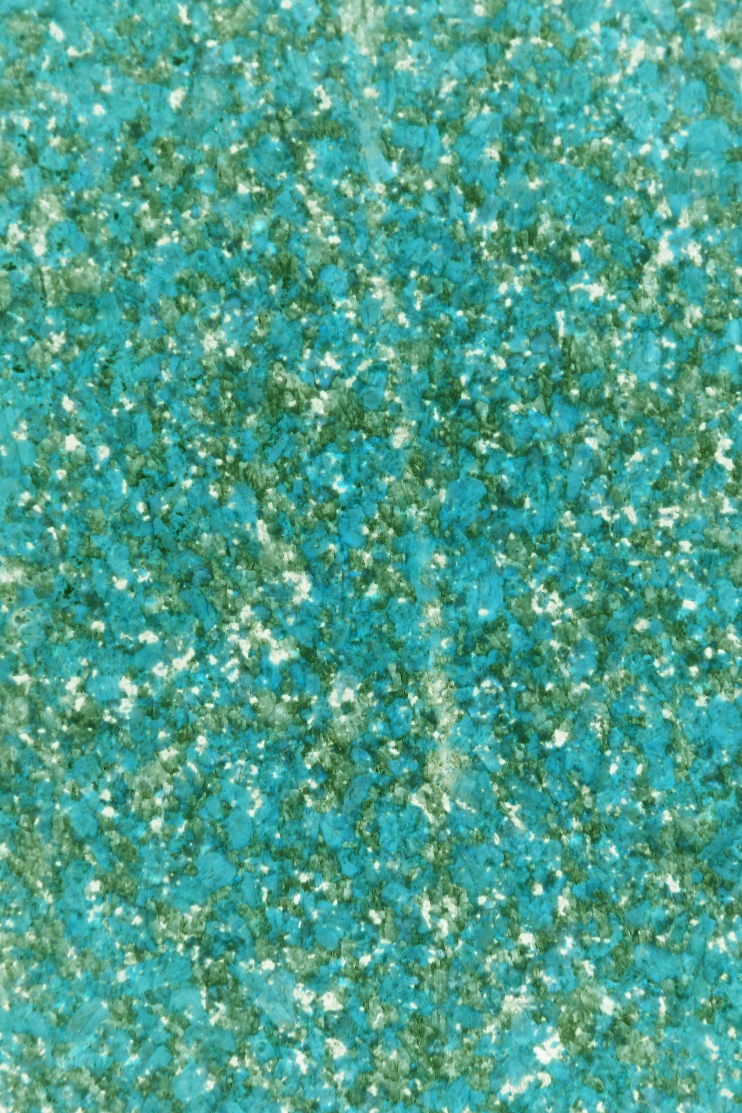 Close-up of a textured surface with blue, green, and white speckles, resembling glitter or a granular material.