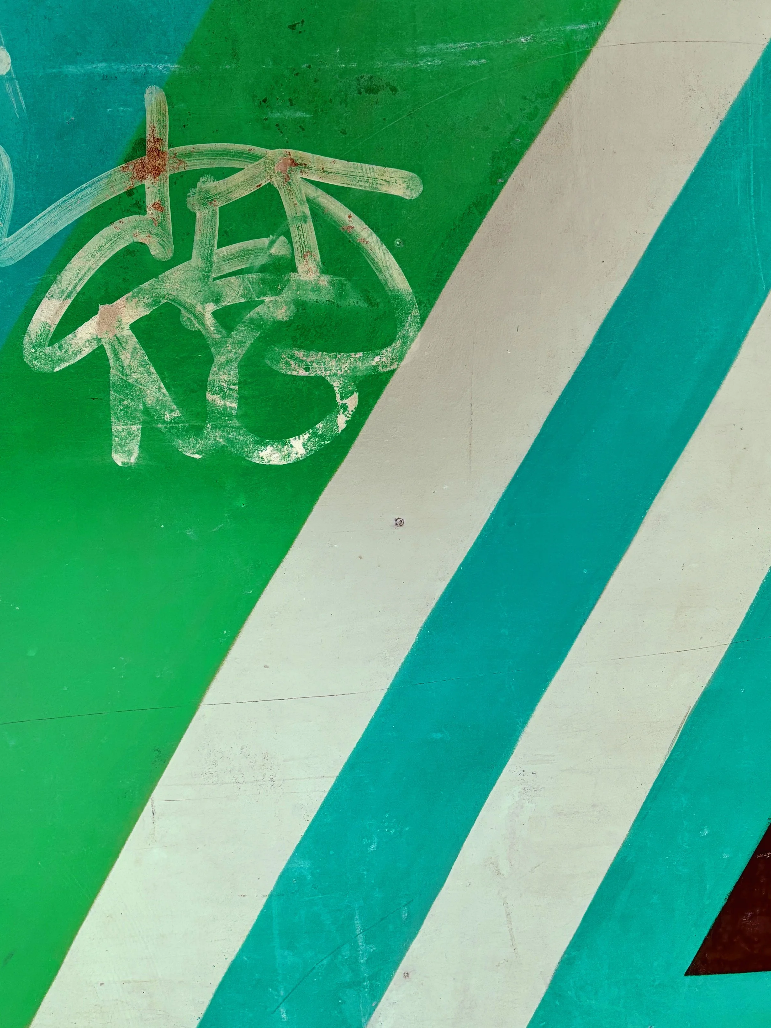 Close-up of a painted surface with diagonal stripes in green, white, and teal. There is a white outline of a bicycle on the surface, with some areas faded or worn.