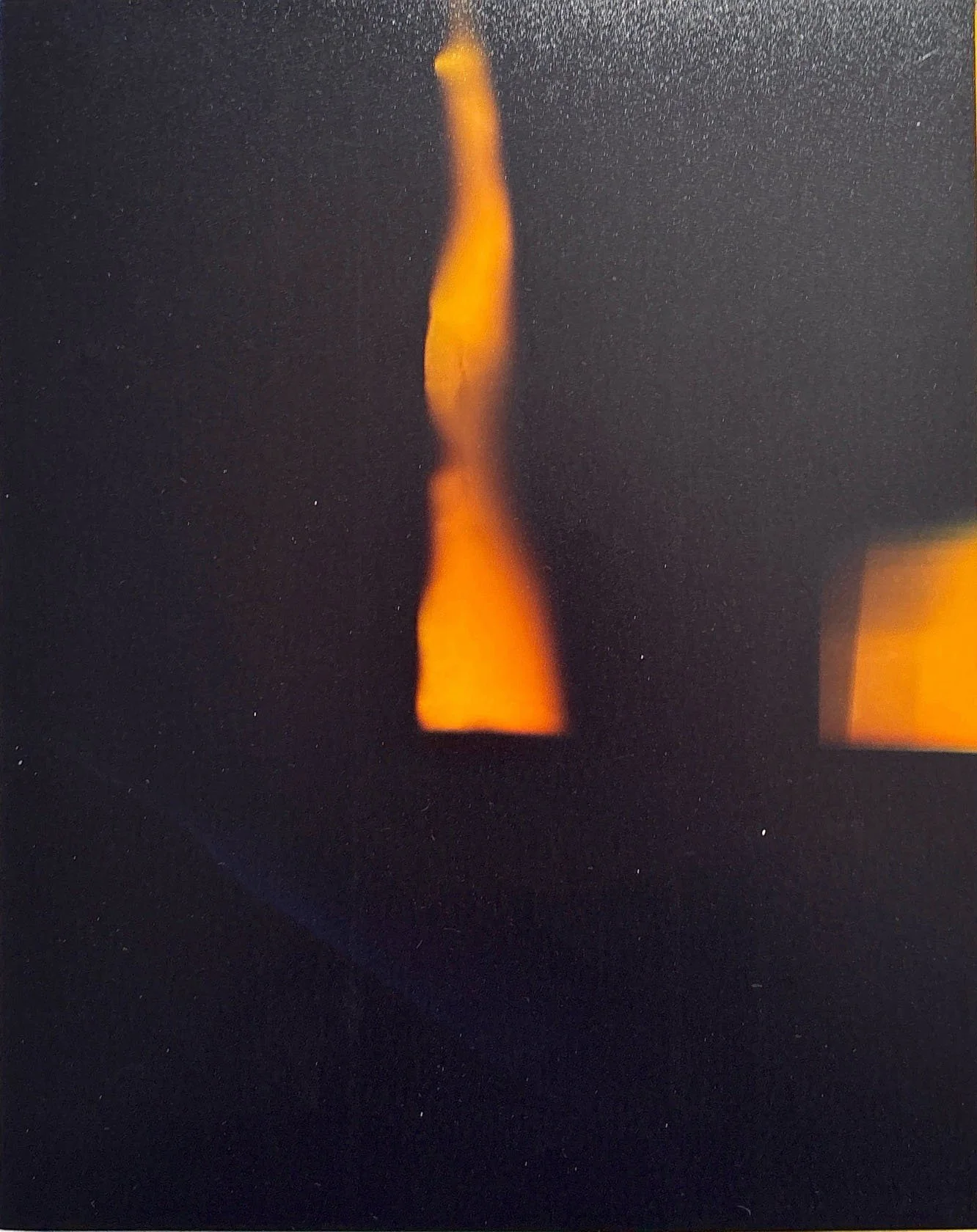 Close-up of a lit candle with orange flame against a dark background.