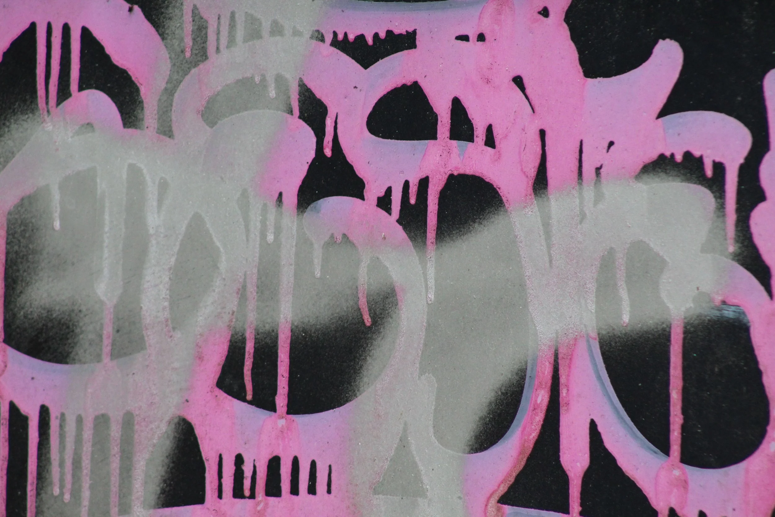 A street art graffiti featuring overlapping skulls in pink and black colors with drips of paint.