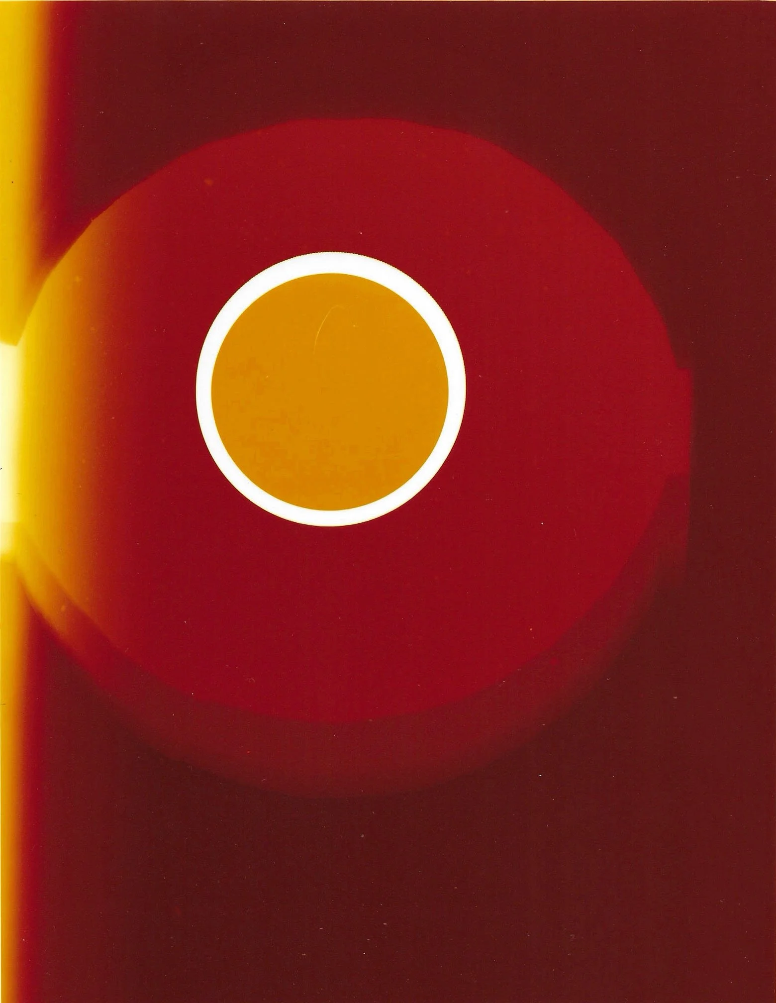 Close-up of a circular object with a white ring inside a larger gold circle against a dark red background.