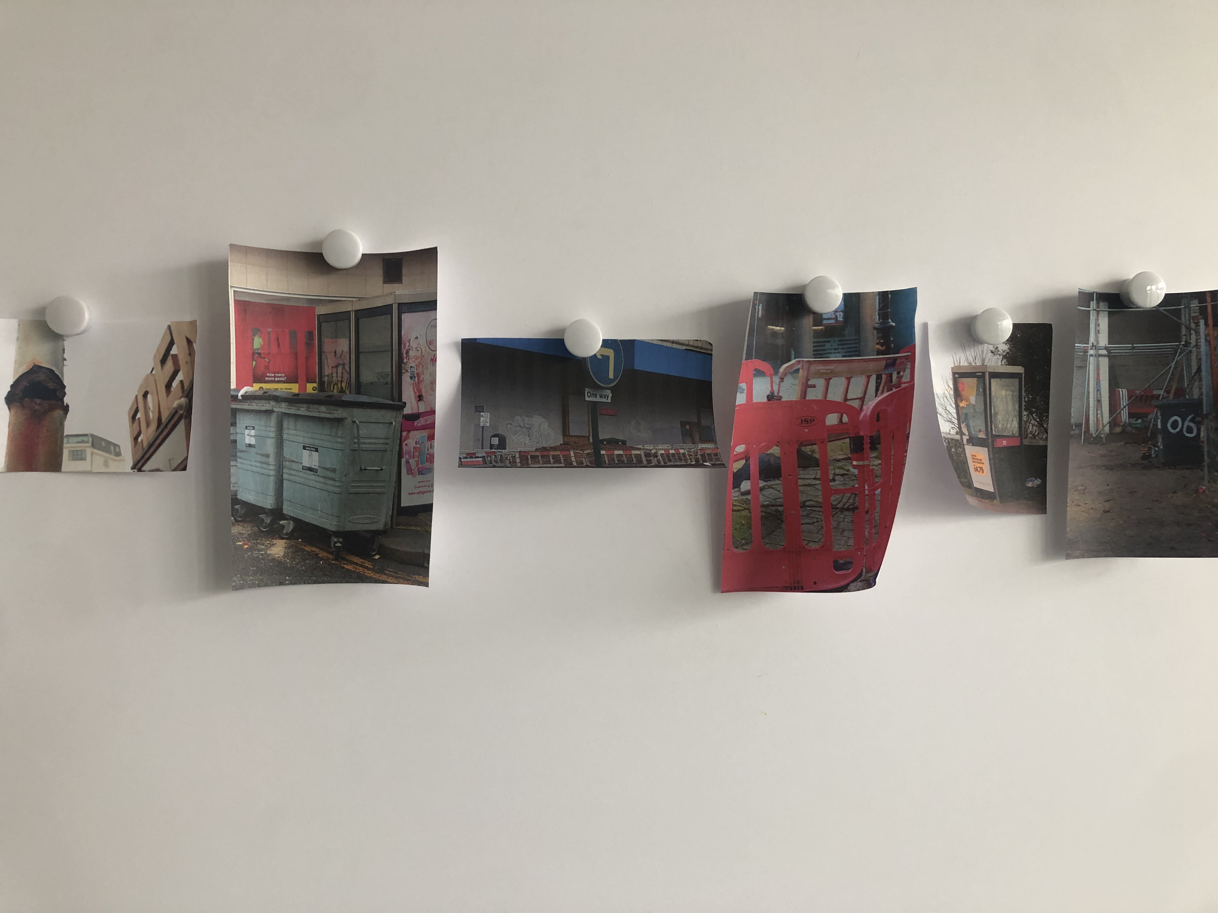 Multiple photographs taped to a white wall, showing various urban scenes and objects such as containers, buildings, and street signs.