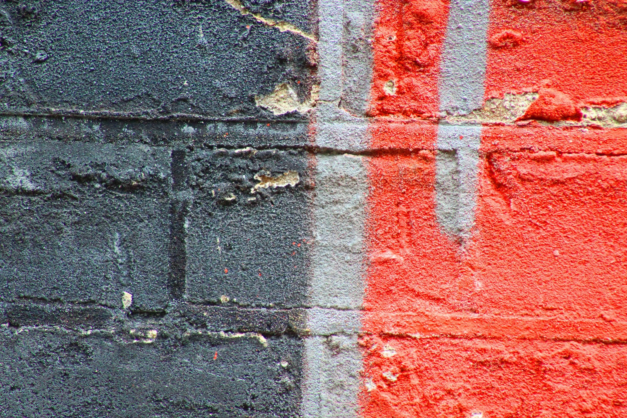 Close-up of a brick wall painted with black and red spray paint, with visible texture and uneven edges.