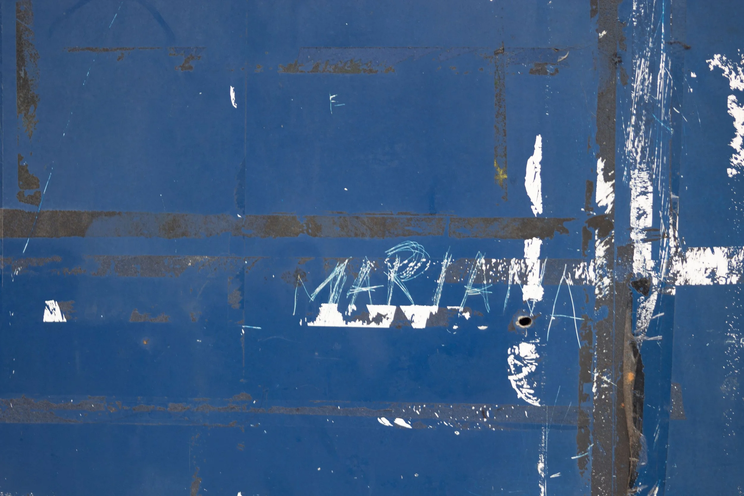 Close-up of a weathered blue metal surface with scratches, paint chipping, and graffiti.