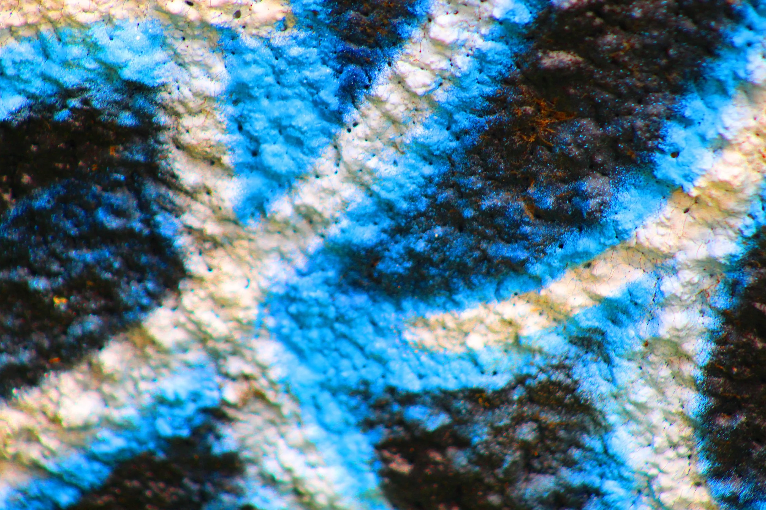 Close-up of a textured, multicolored surface with patches of blue, black, and pink, resembling a rough, rocky material.
