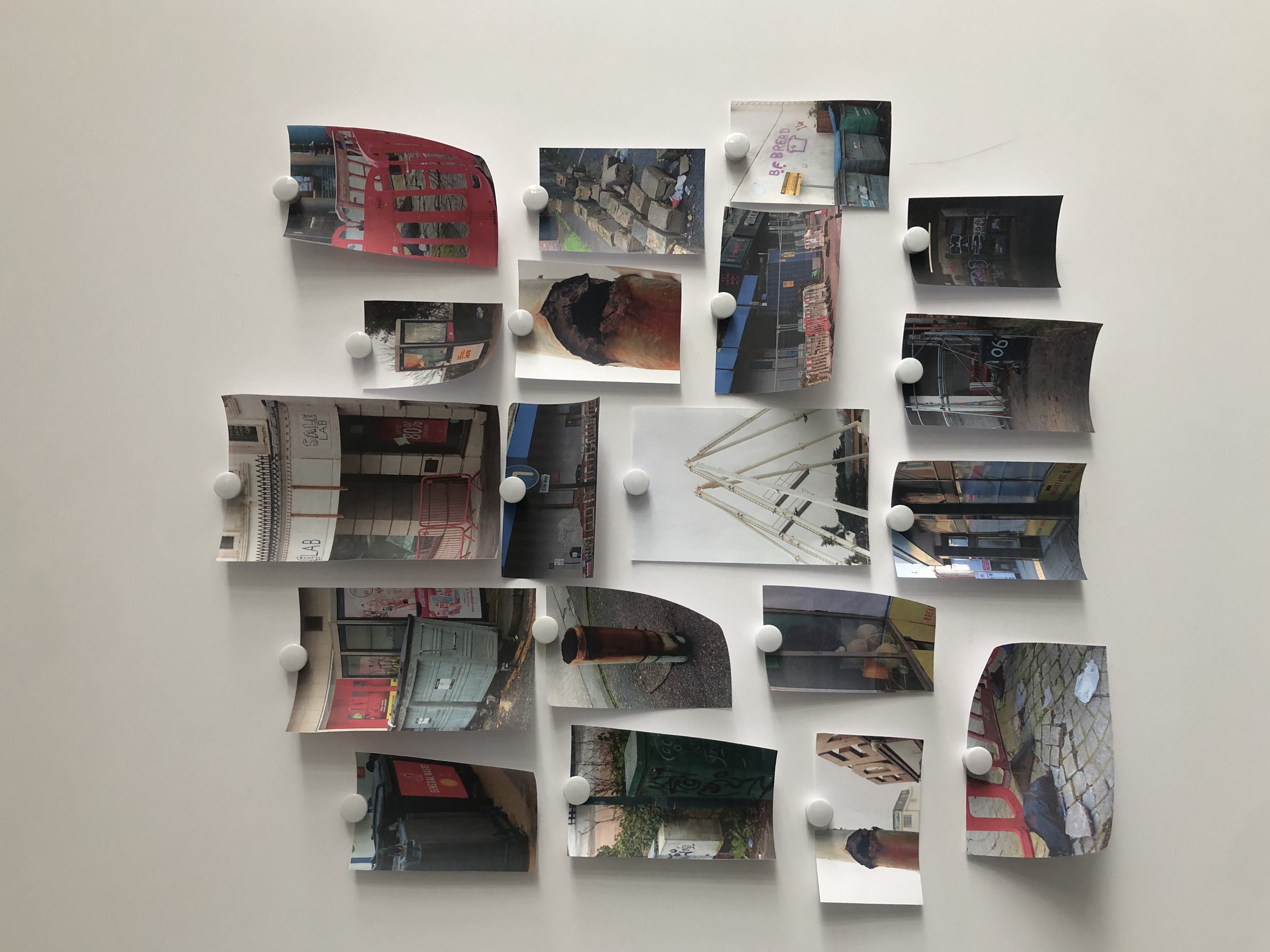 Arranged photographs on a wall held by white round magnets displaying urban scenes, storefronts, street views, and construction sites.