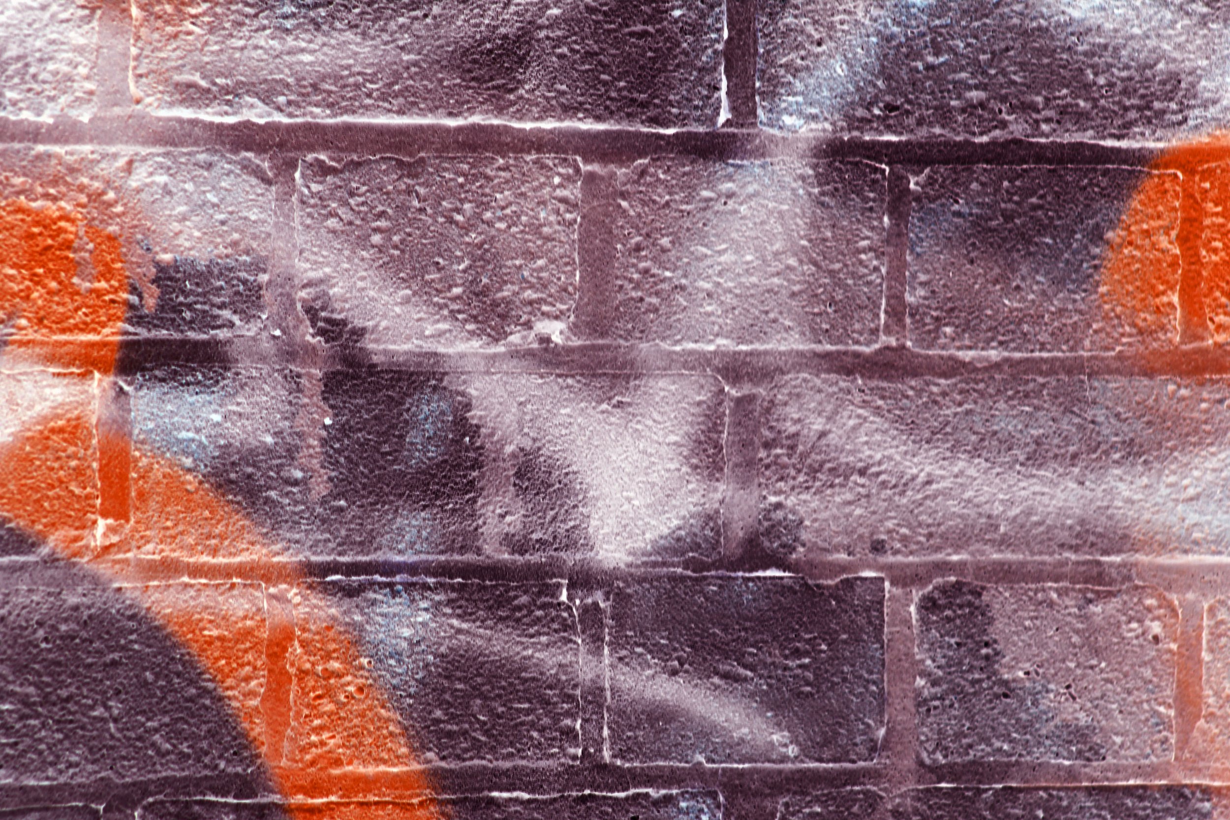 Close-up of a brick wall with orange graffiti spray paint.