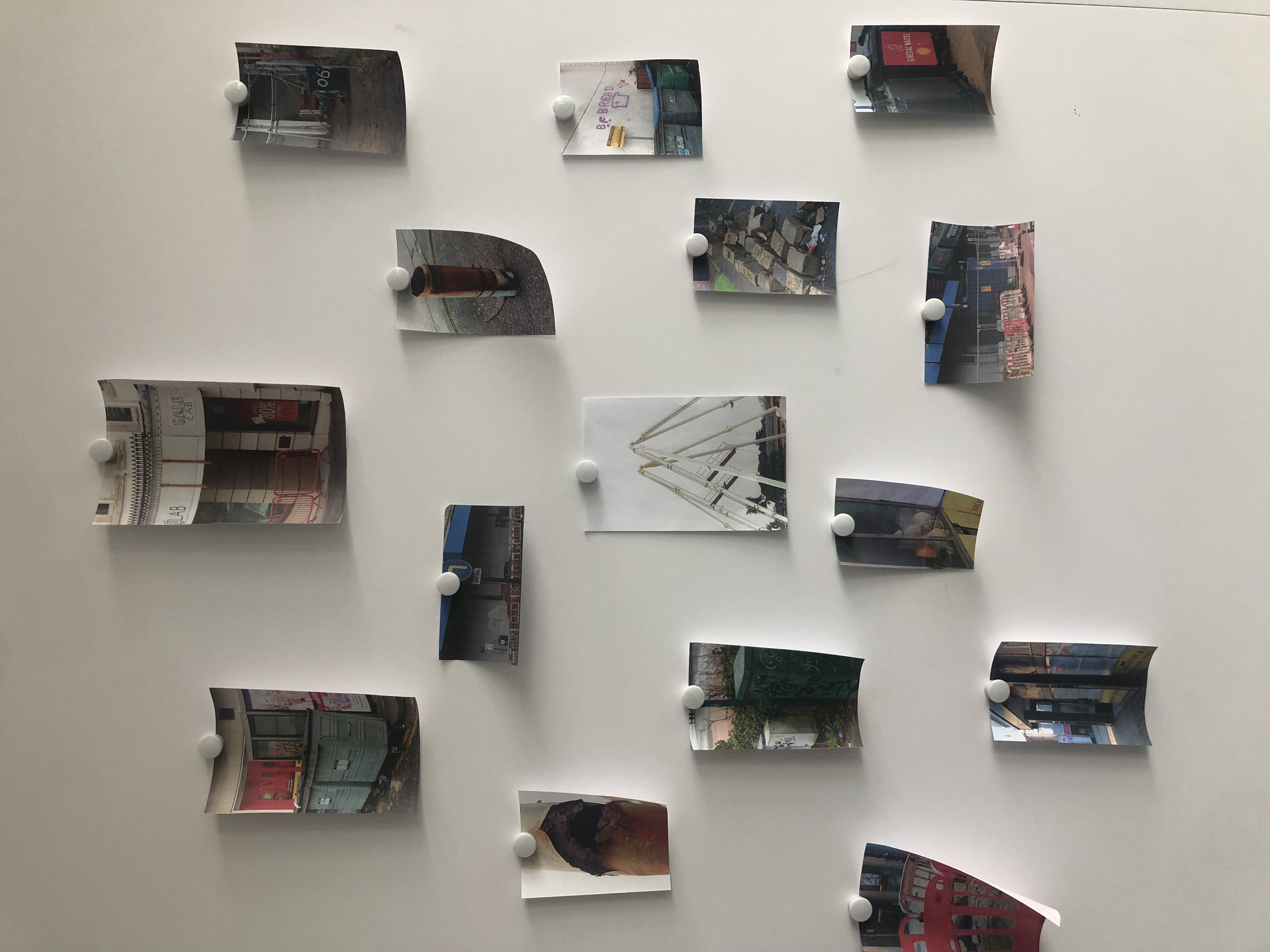 A collection of photographs of urban street scenes and architecture, displayed on a white wall with thumbtacks.