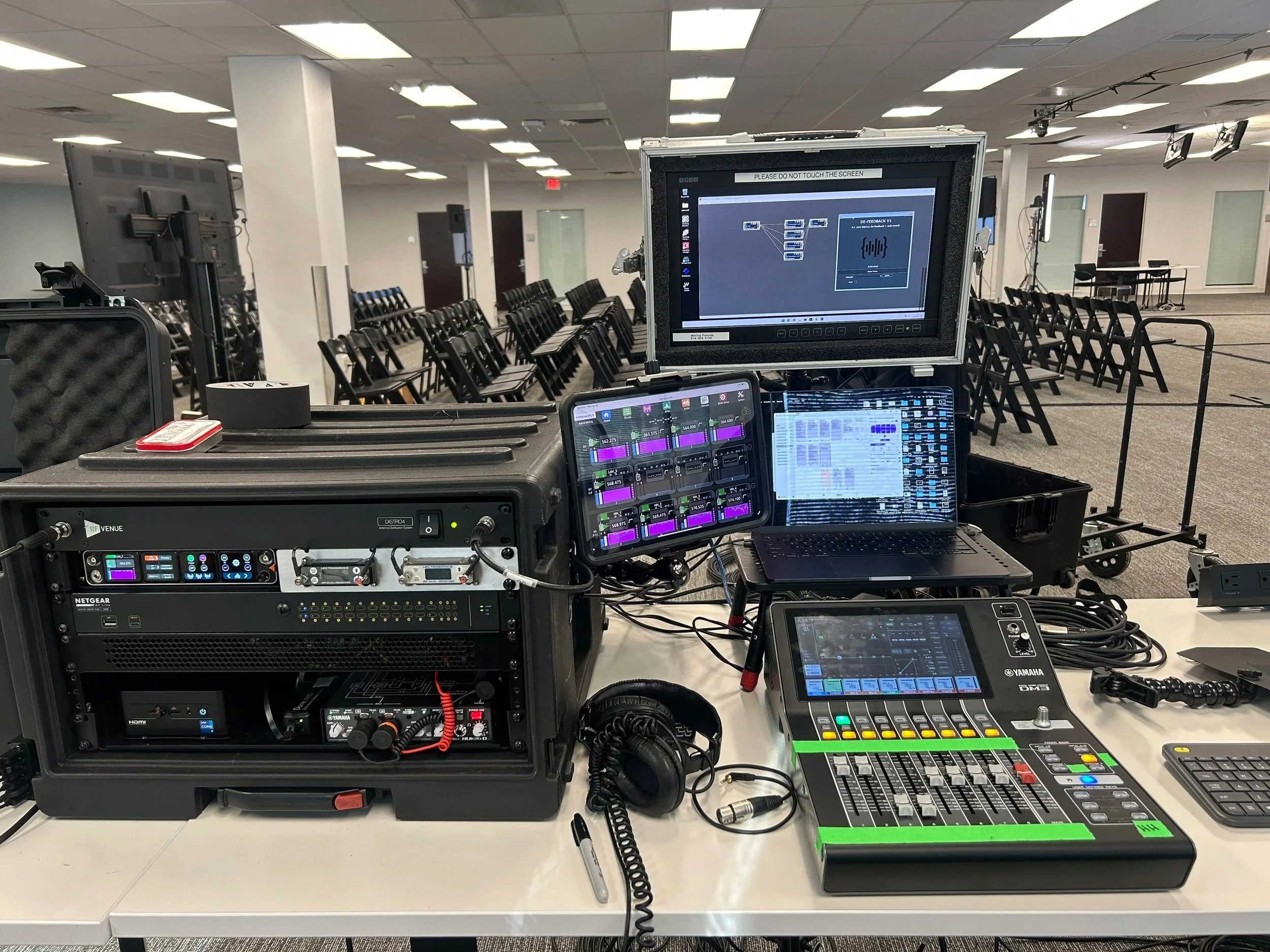 Audio and video mixing equipment set up in a conference room with chairs arranged in rows, projection screens, and ceiling lights.