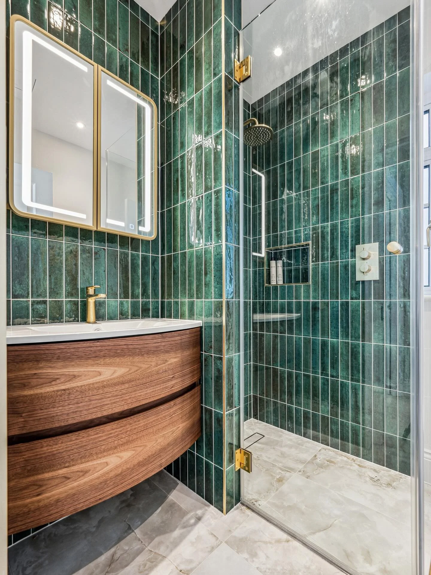 Elegance in compact form. 

Rich, bottle green vertical tiles meet American Walnut curves and brushed brass fittings, creating a serene, immersive experience in this small but striking en suite